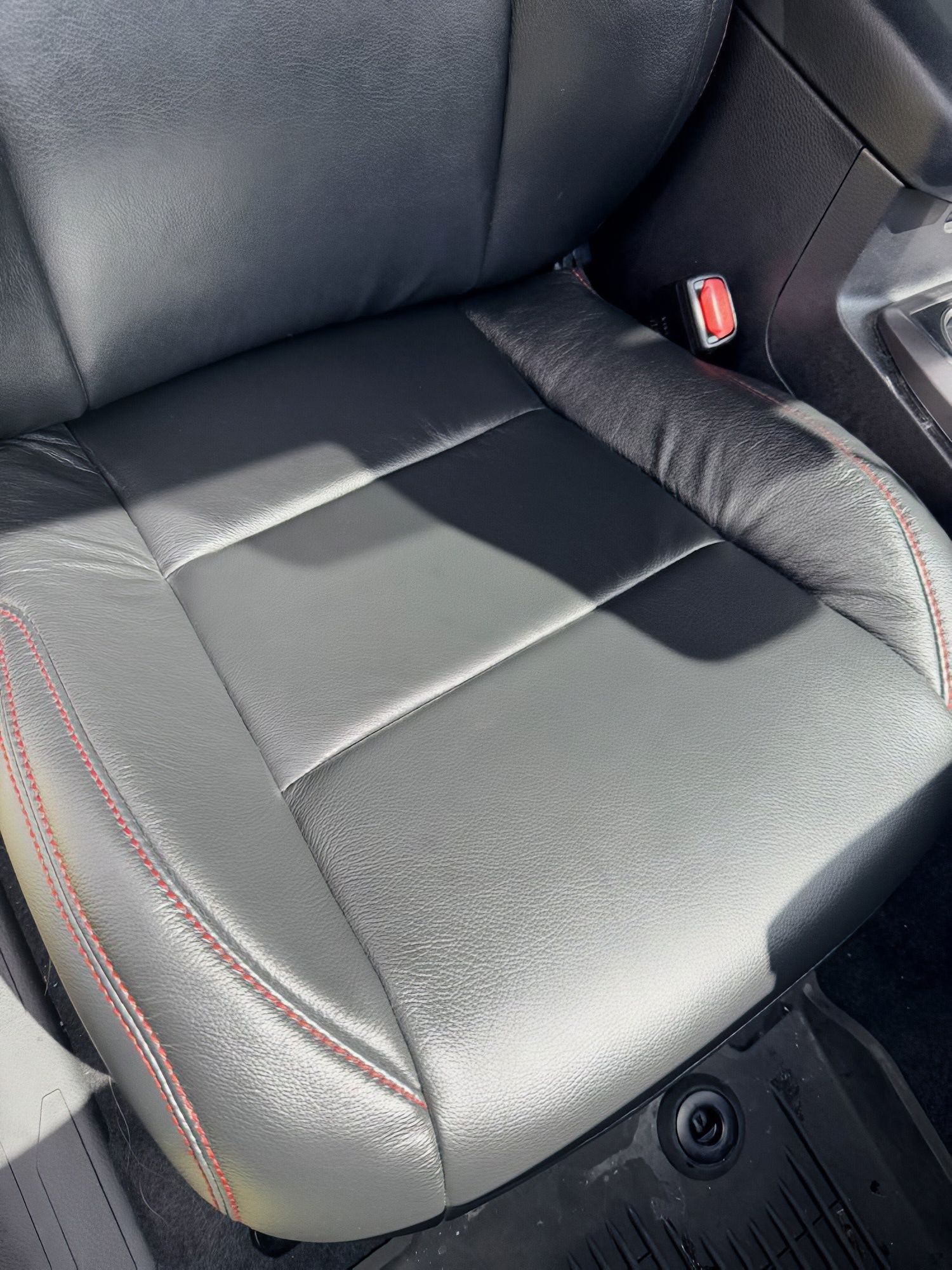 Black leather car seat with red stitching and a visible seatbelt buckle.