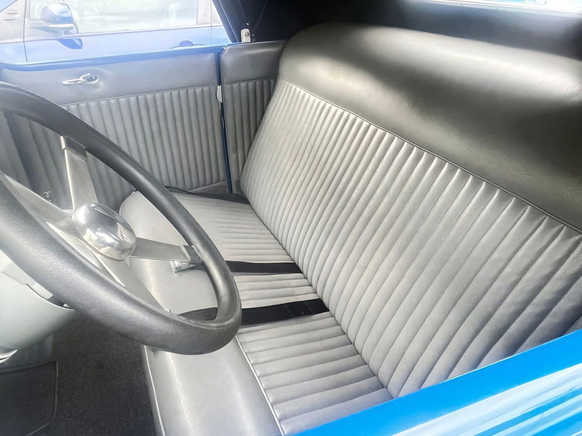 Front seat of a vintage car with gray vinyl upholstery and a black steering wheel