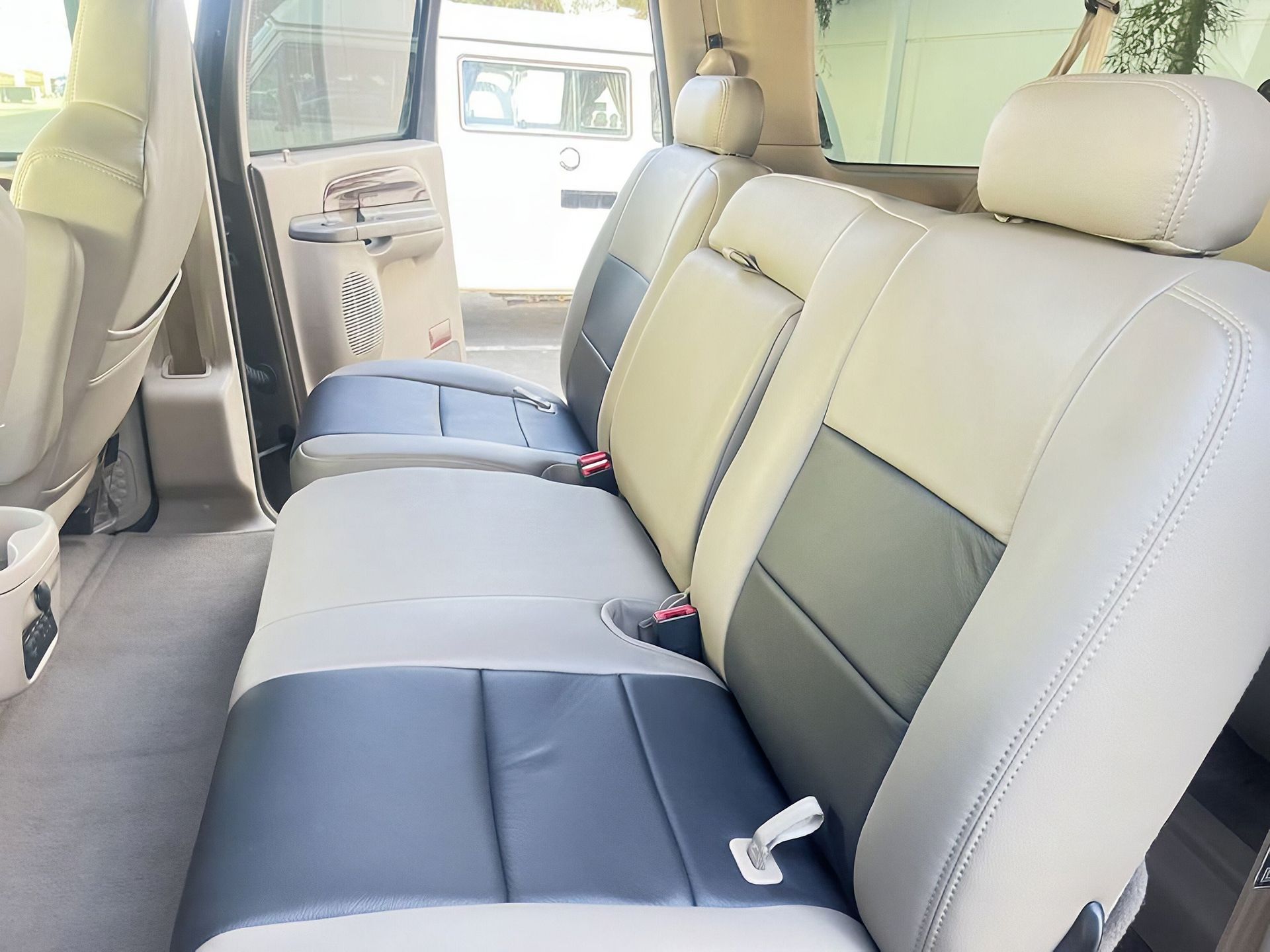 Light beige and black car back seat interior with three headrests and open door view