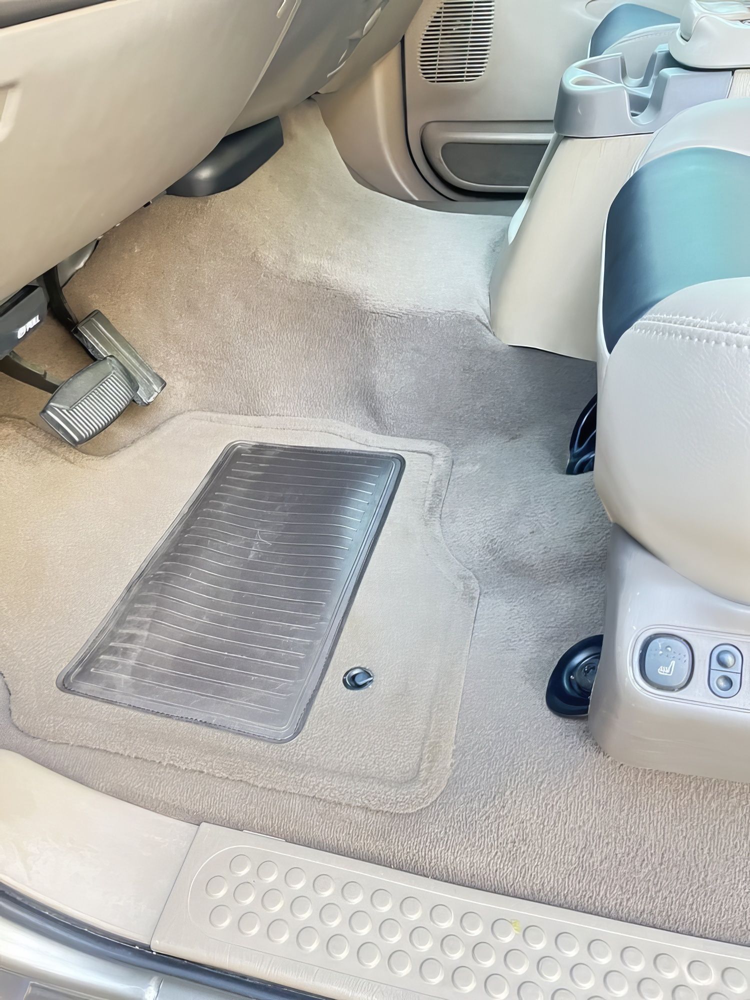 Car interior footwell with beige carpet, floor mat, and front seat adjustment controls