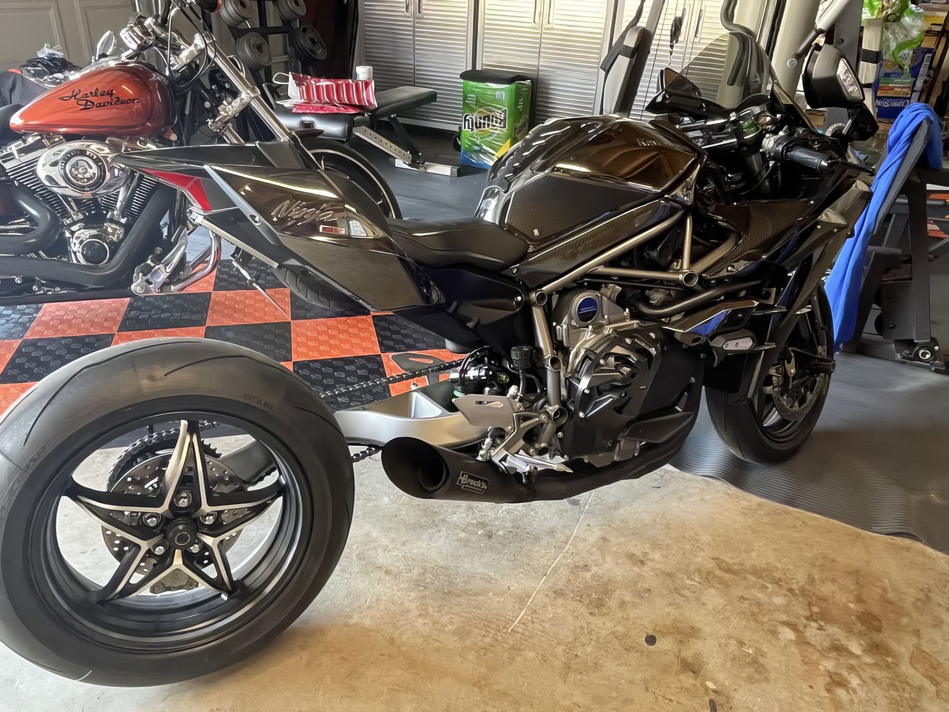 Black motorcycle with a detached front wheel in a garage, near another bike and a red-and-black floor mat