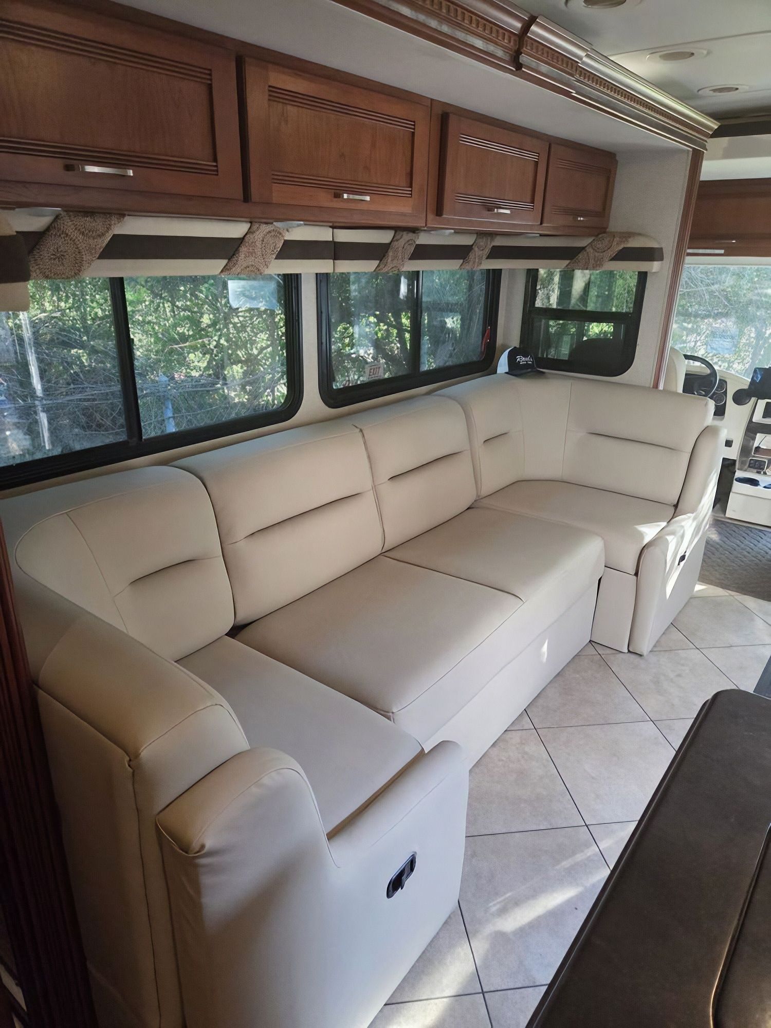 Cream leather sofa in an RV interior with wood cabinets and large windows.