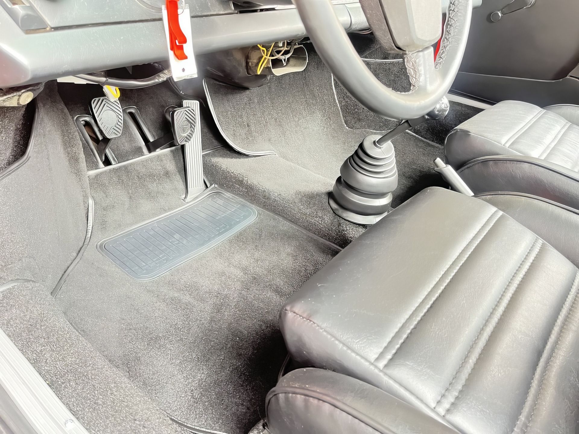 Car interior with steering wheel, pedals, manual gear shifter, and black seats