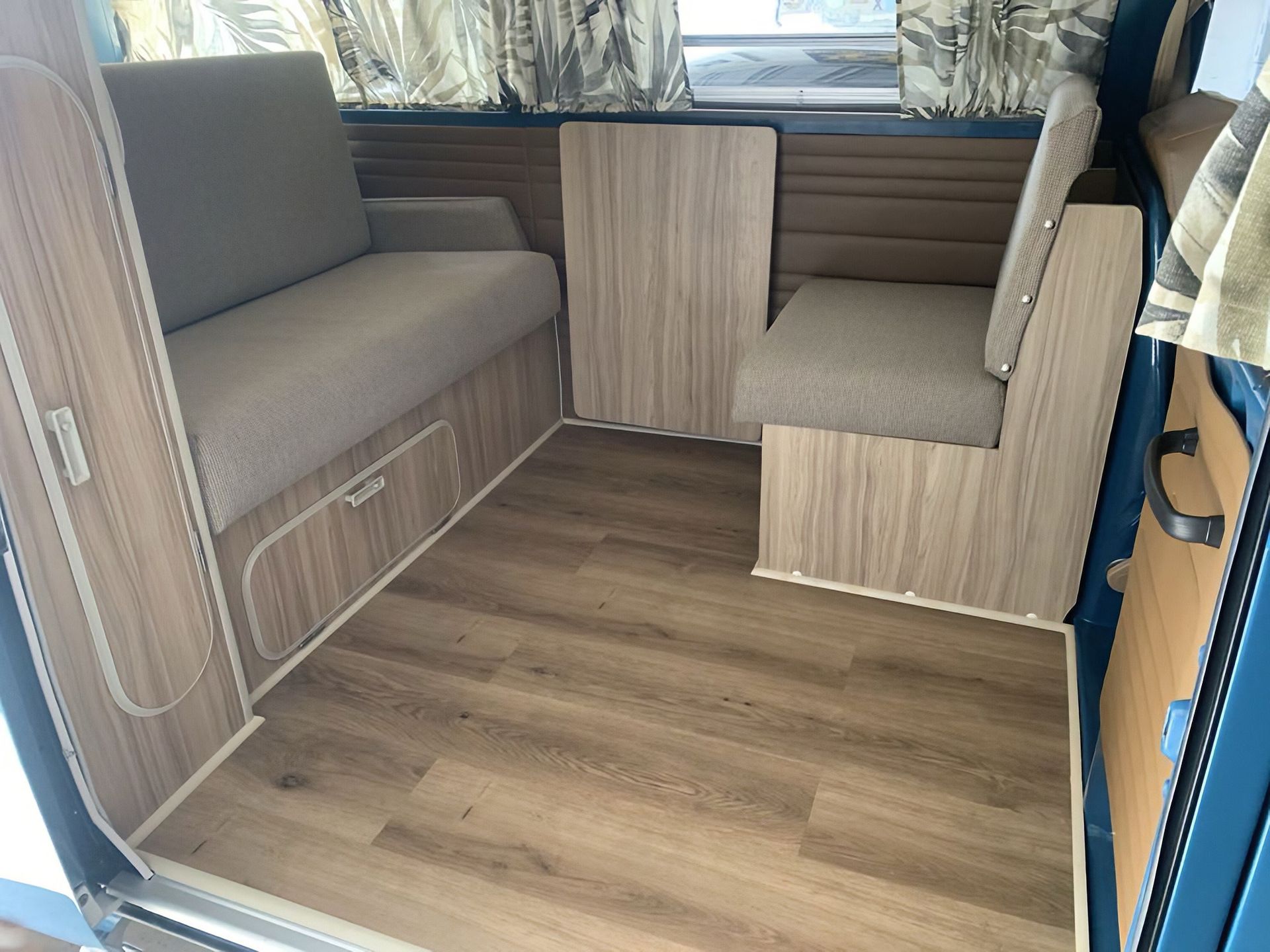 Small camper van interior with gray bench seats, wood paneling, and a wood-look floor.