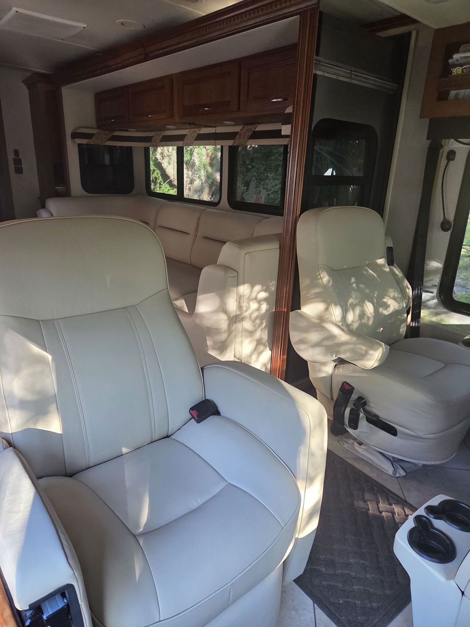 RV interior with beige captain’s chairs, wood cabinets, and windows letting in daylight