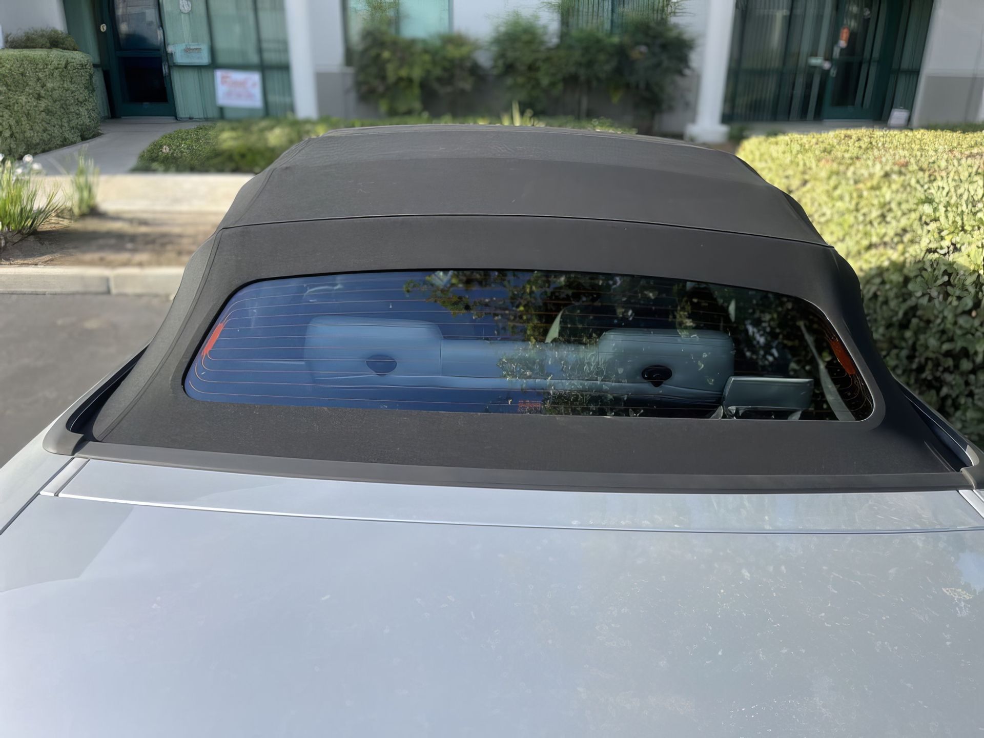 Rear view of a silver convertible with a black soft top parked outside a building