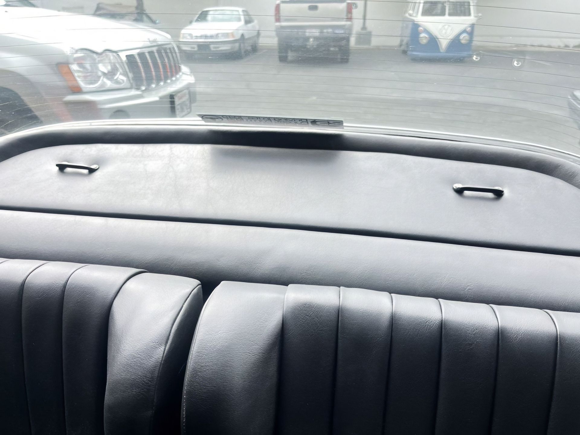 View from a car's back seat through the rear window at a parking lot with several parked vehicles.