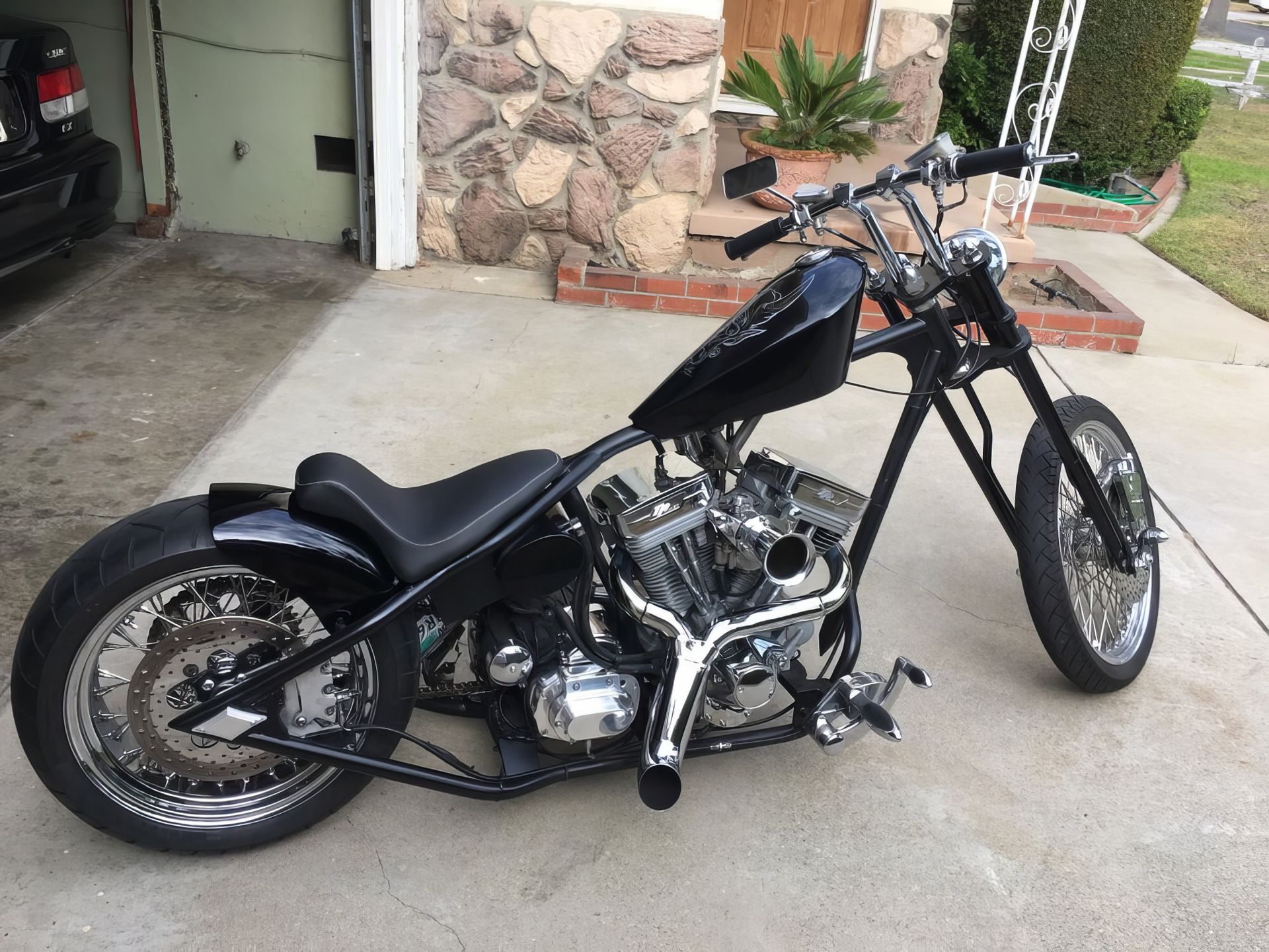 Black custom chopper motorcycle parked on a driveway in front of a house