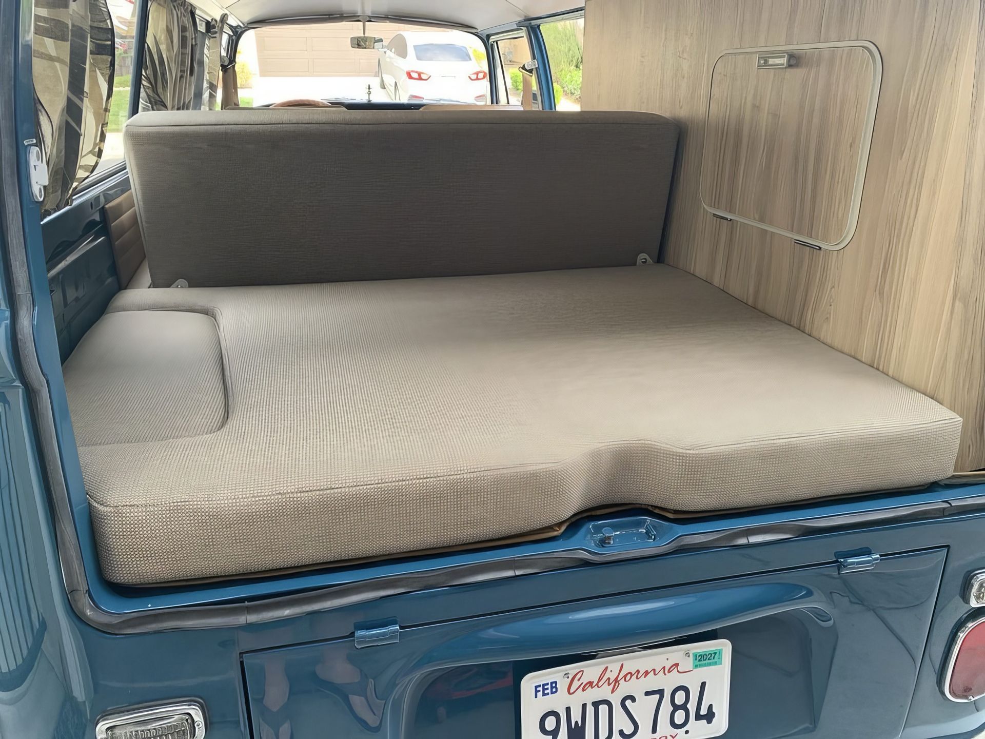 Back of a blue van with a beige mattress-style cargo bed and California license plate visible