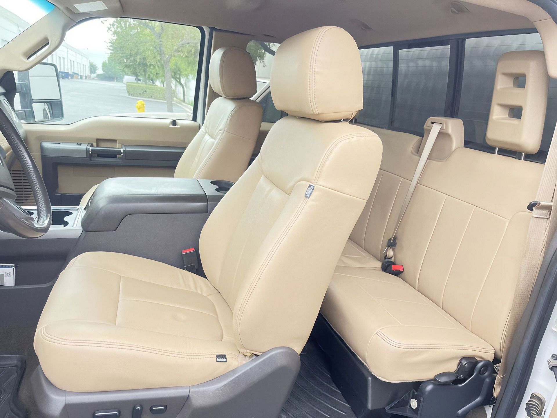 Tan leather truck interior with front seats and rear bench, seen from the open passenger side
