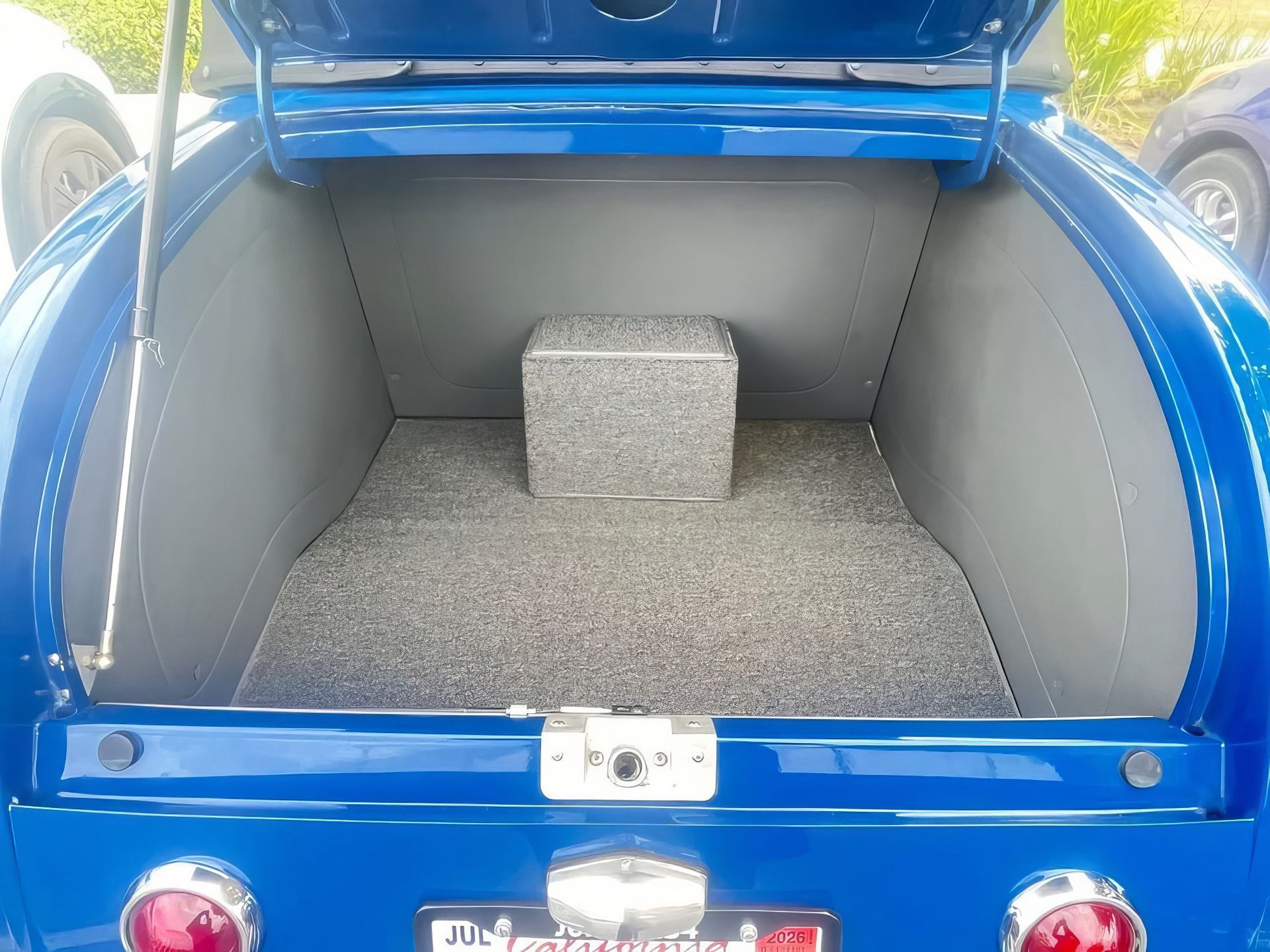 Blue car trunk lined with gray carpet, open and empty except for a small gray box in the center.