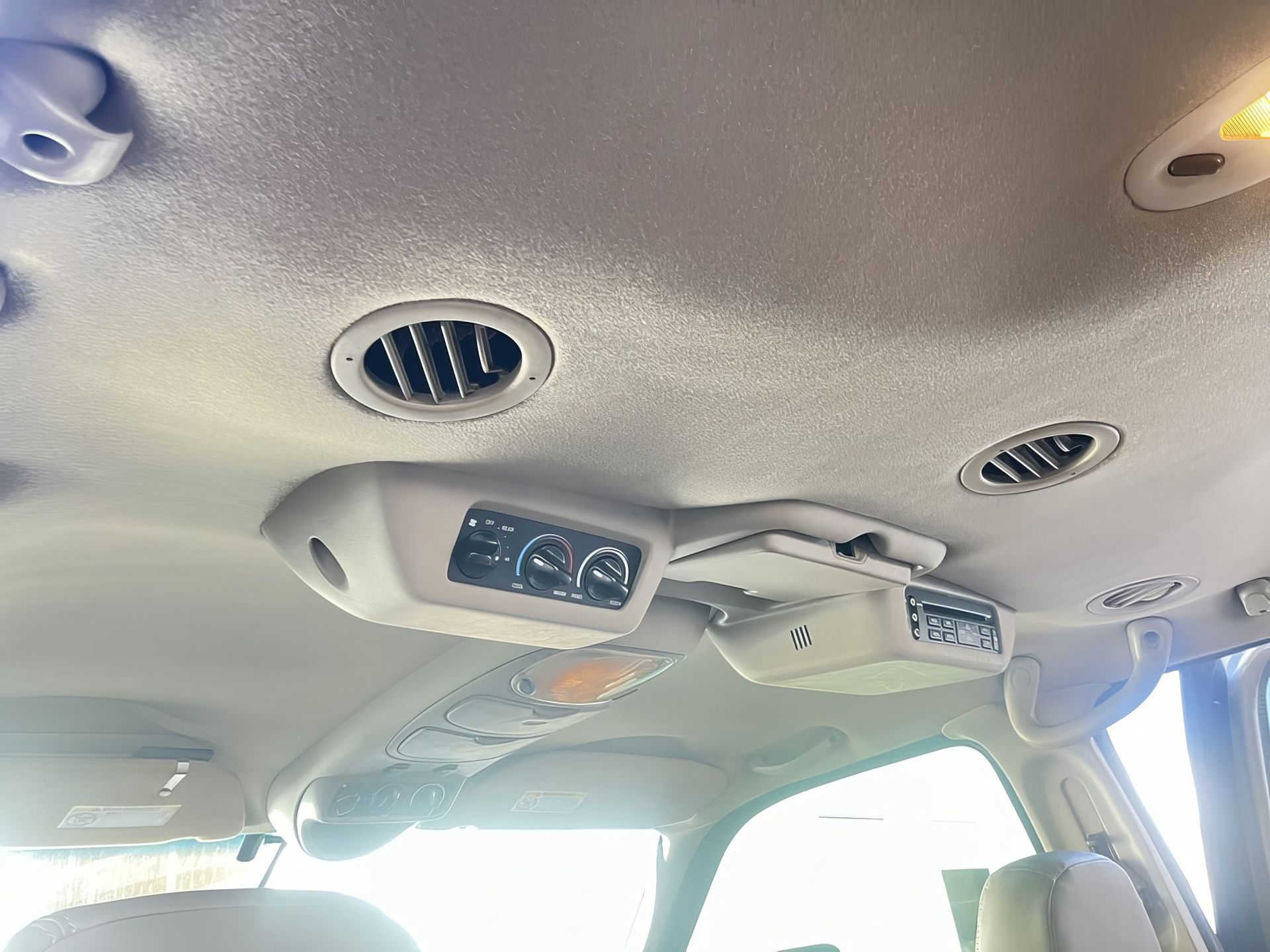 Car interior ceiling with air vents, overhead controls, and bright daylight through the windows