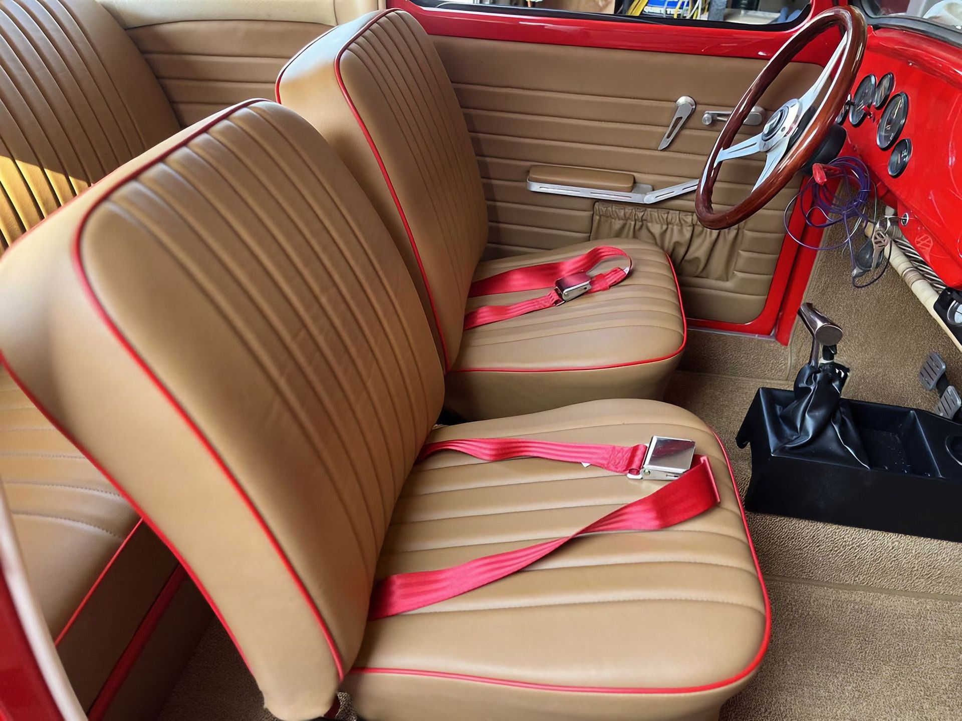 Tan car interior with red accents, two front seats, steering wheel, and red seat belts