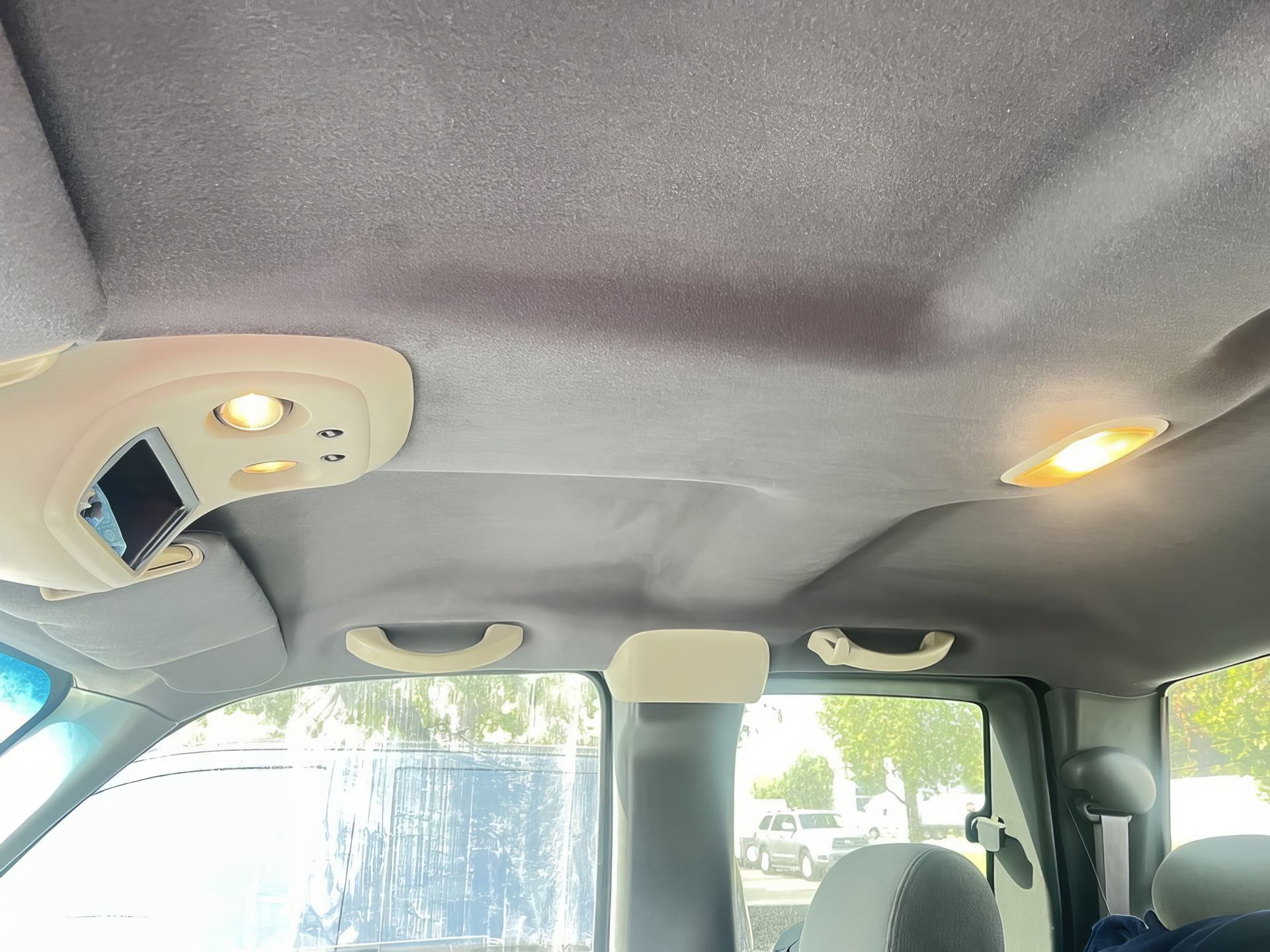 Interior of a vehicle with gray ceiling, dome lights on, and bright daylight through the windows.