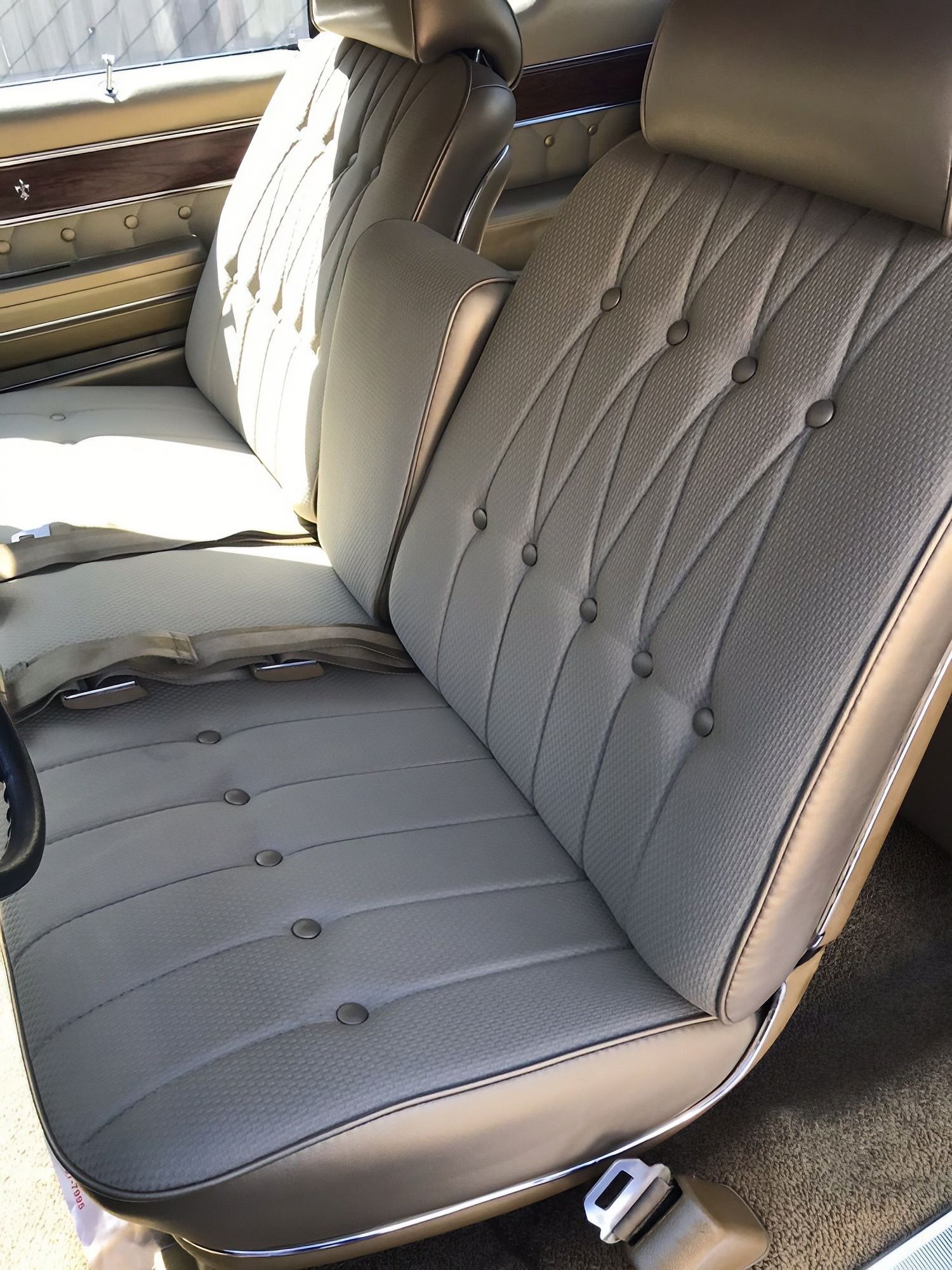 Gray tufted car bench seat with tan trim and seat belt buckles in a vintage interior