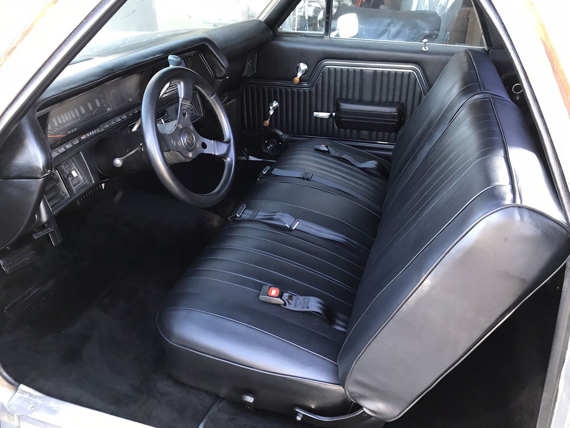 Black car interior with bucket seats, steering wheel, and striped bench seat in the back.