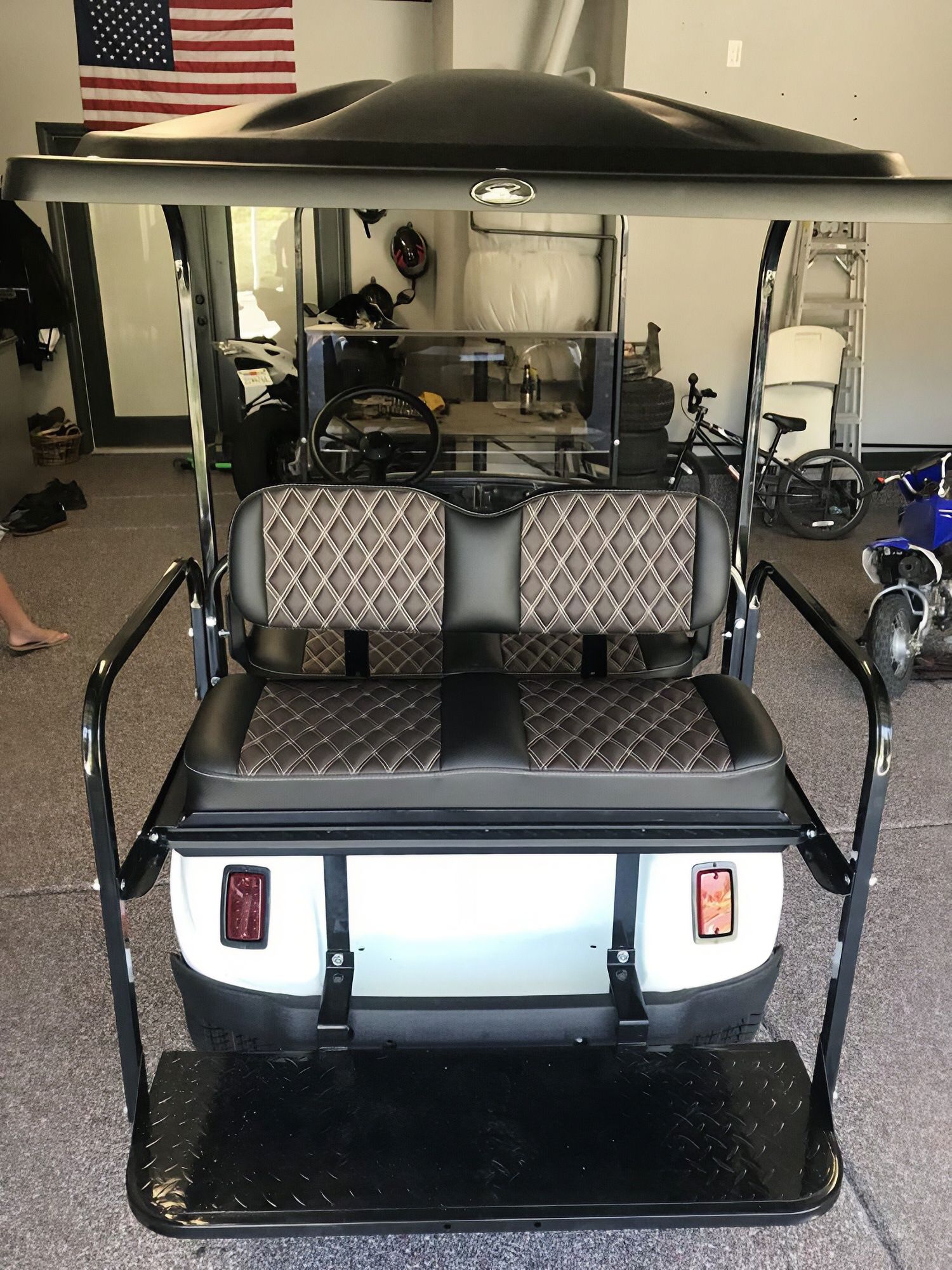 Lifted golf cart with black canopy and brown seats, parked indoors in a garage.