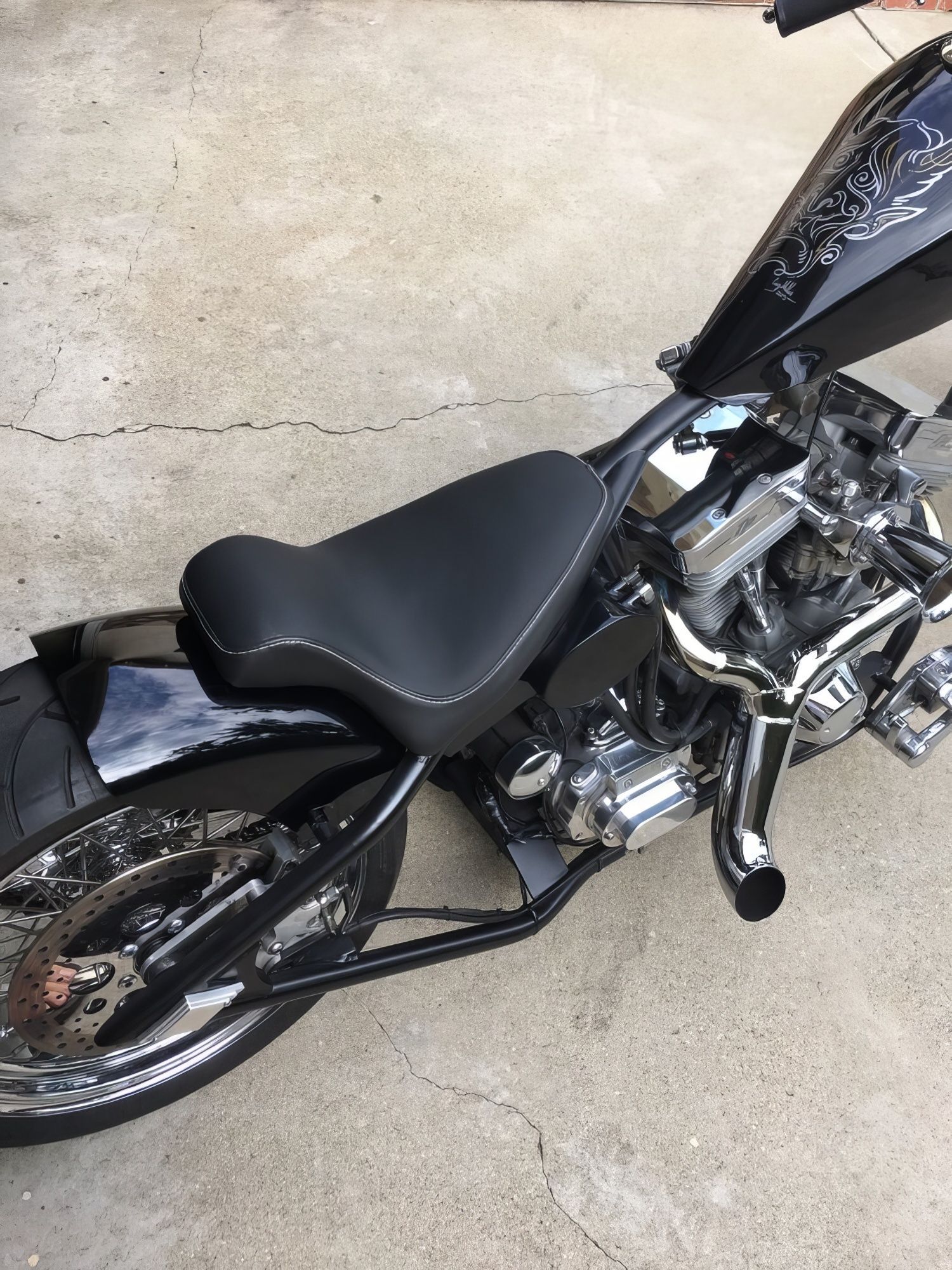 Black motorcycle with a custom seat parked on a concrete surface.