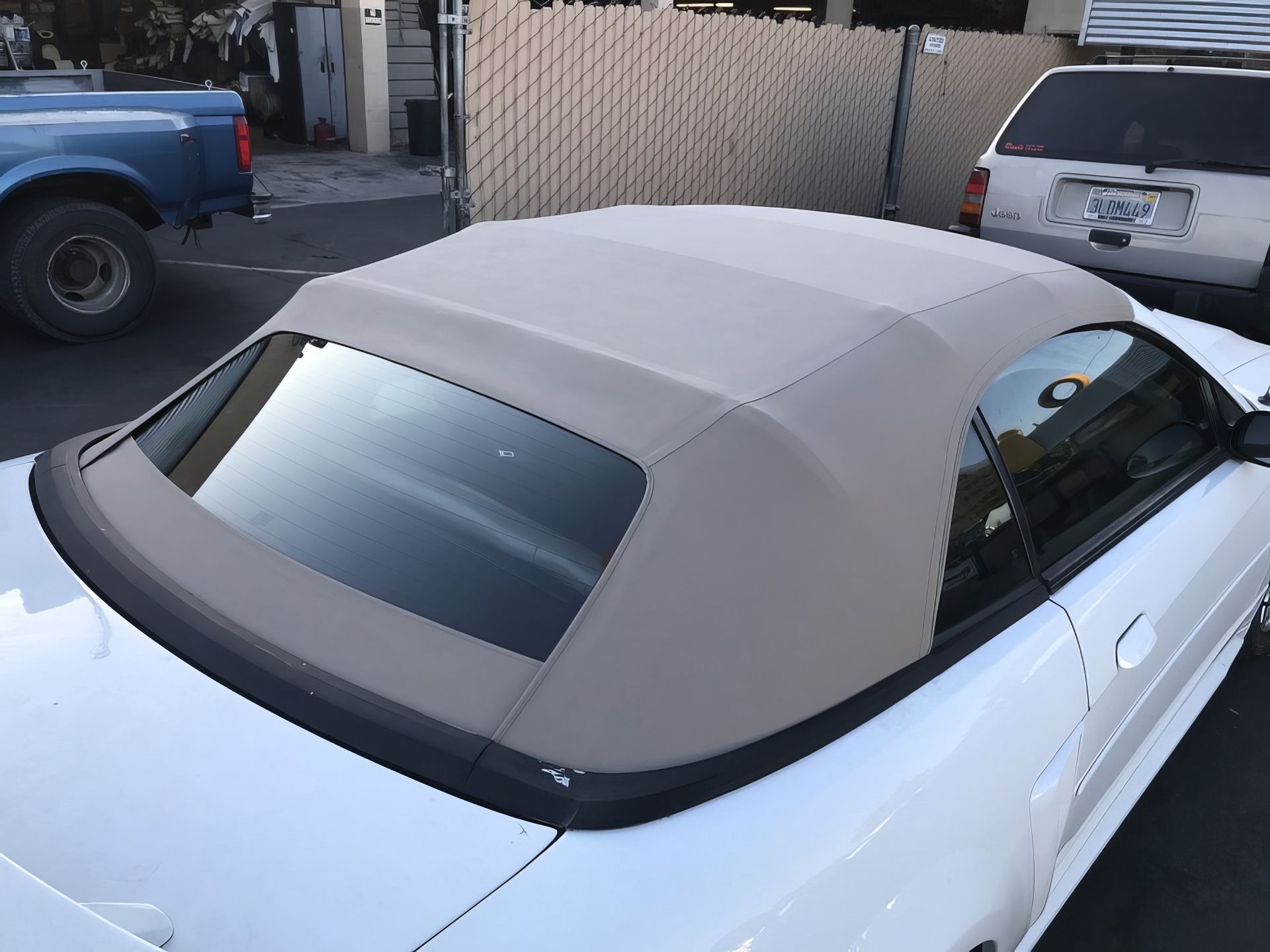 White car with a beige convertible top parked in a lot, viewed from above and behind