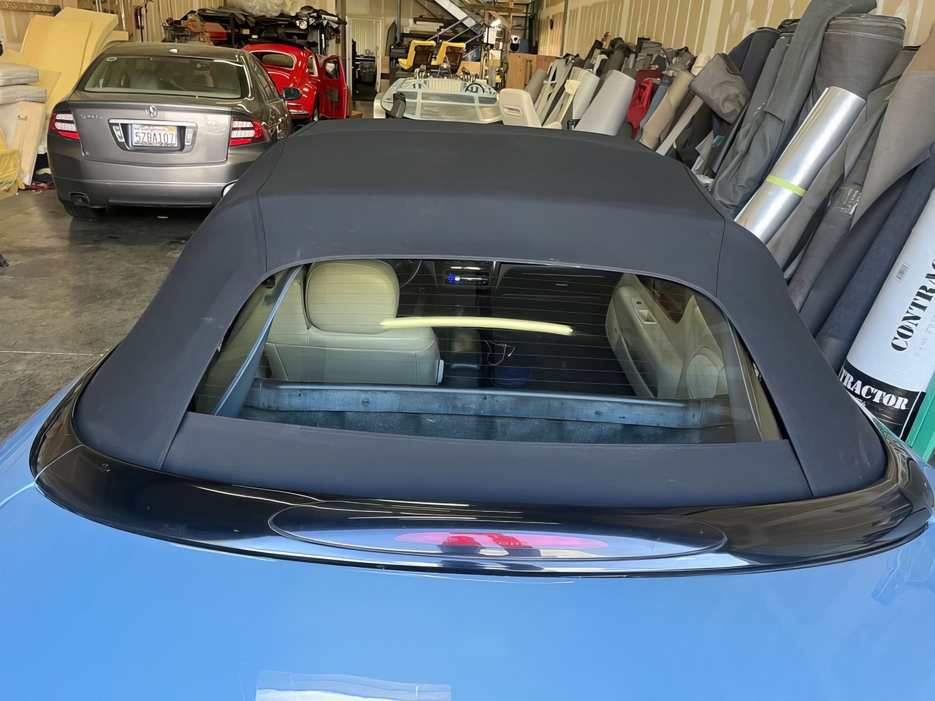 Blue convertible with black soft top parked in a cluttered garage behind a silver sedan
