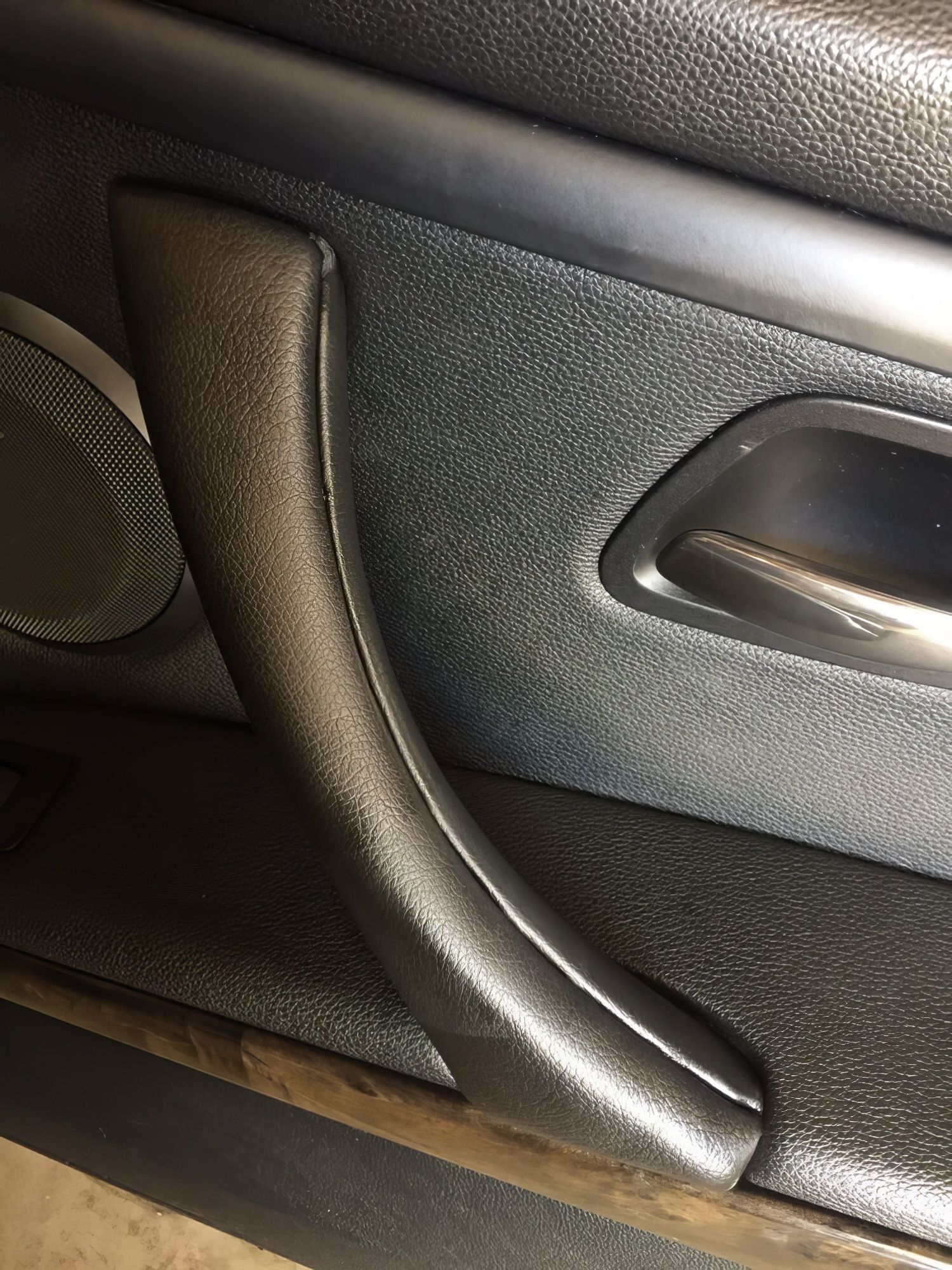 Close-up of a car door interior with black textured panel, handle, and armrest.