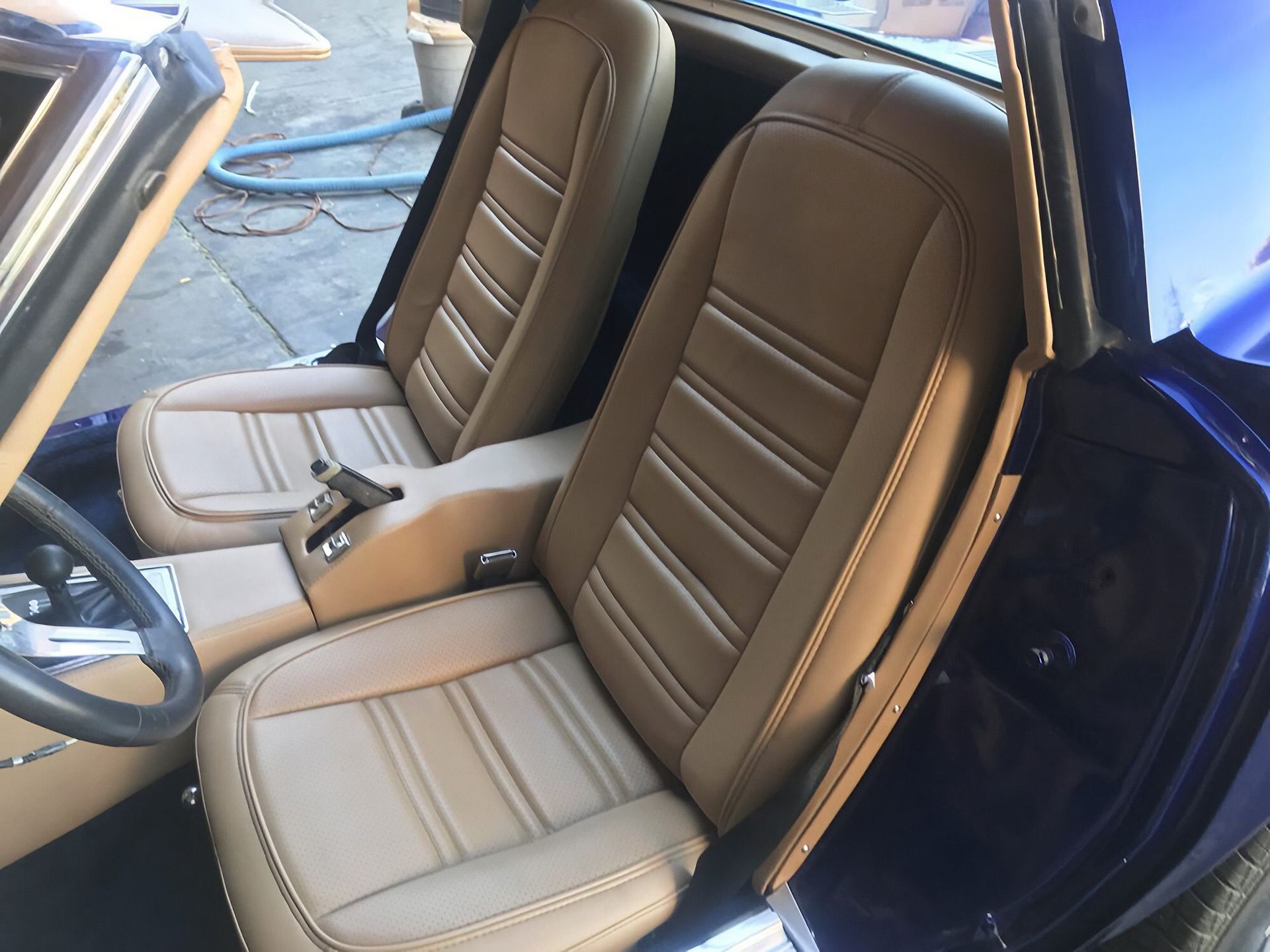Tan leather car seats with center console inside a blue classic car, viewed through the open door