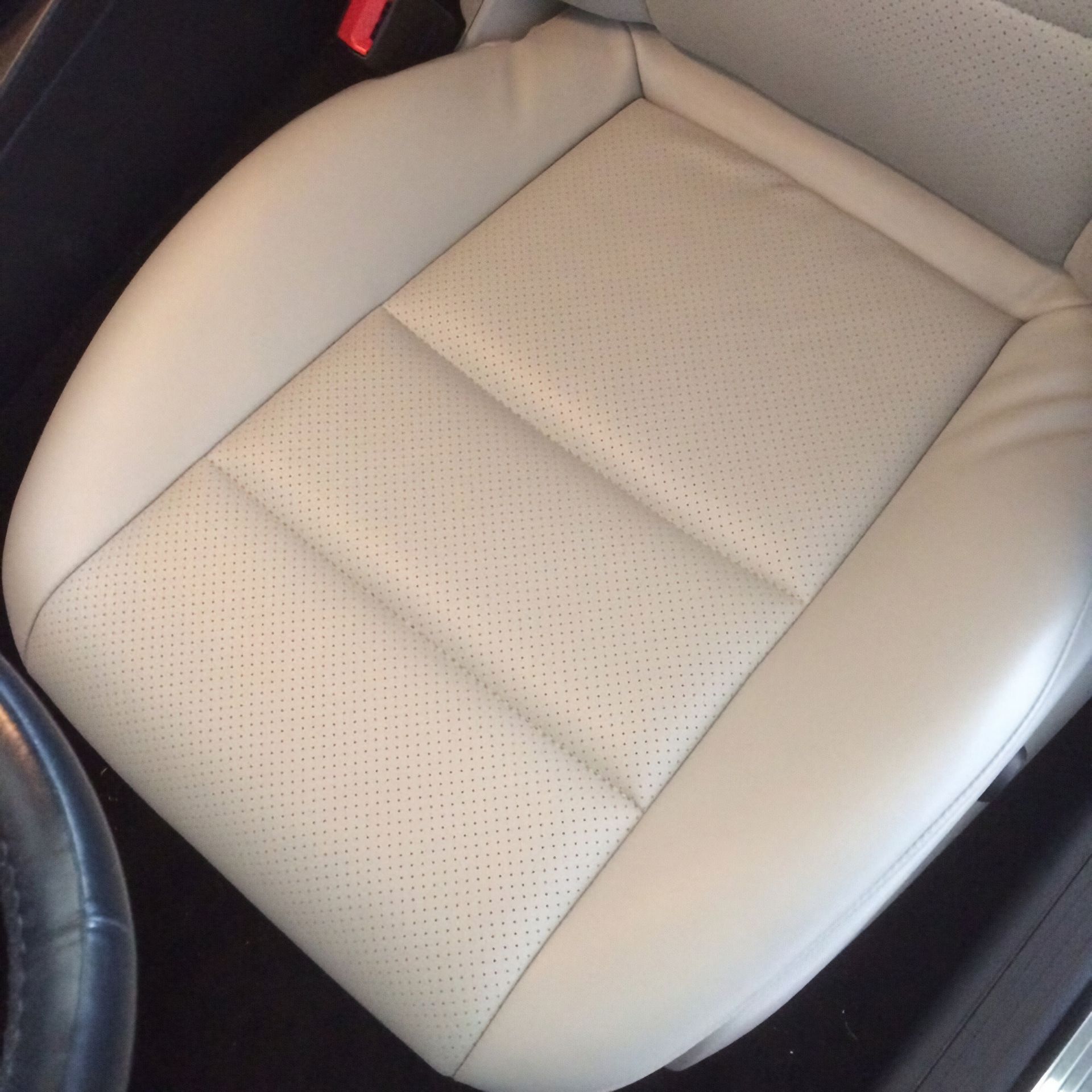 Close-up of a beige perforated car seat cushion with gray side bolsters and black trim.