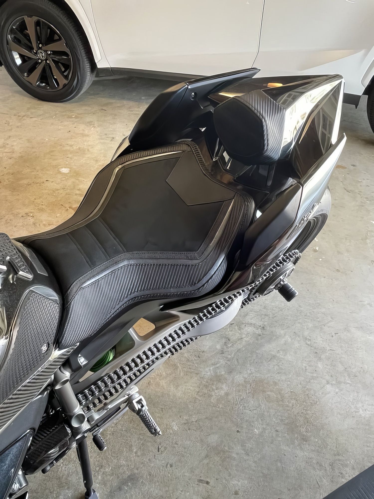 Black motorcycle seat and rear section parked in a garage beside a white car