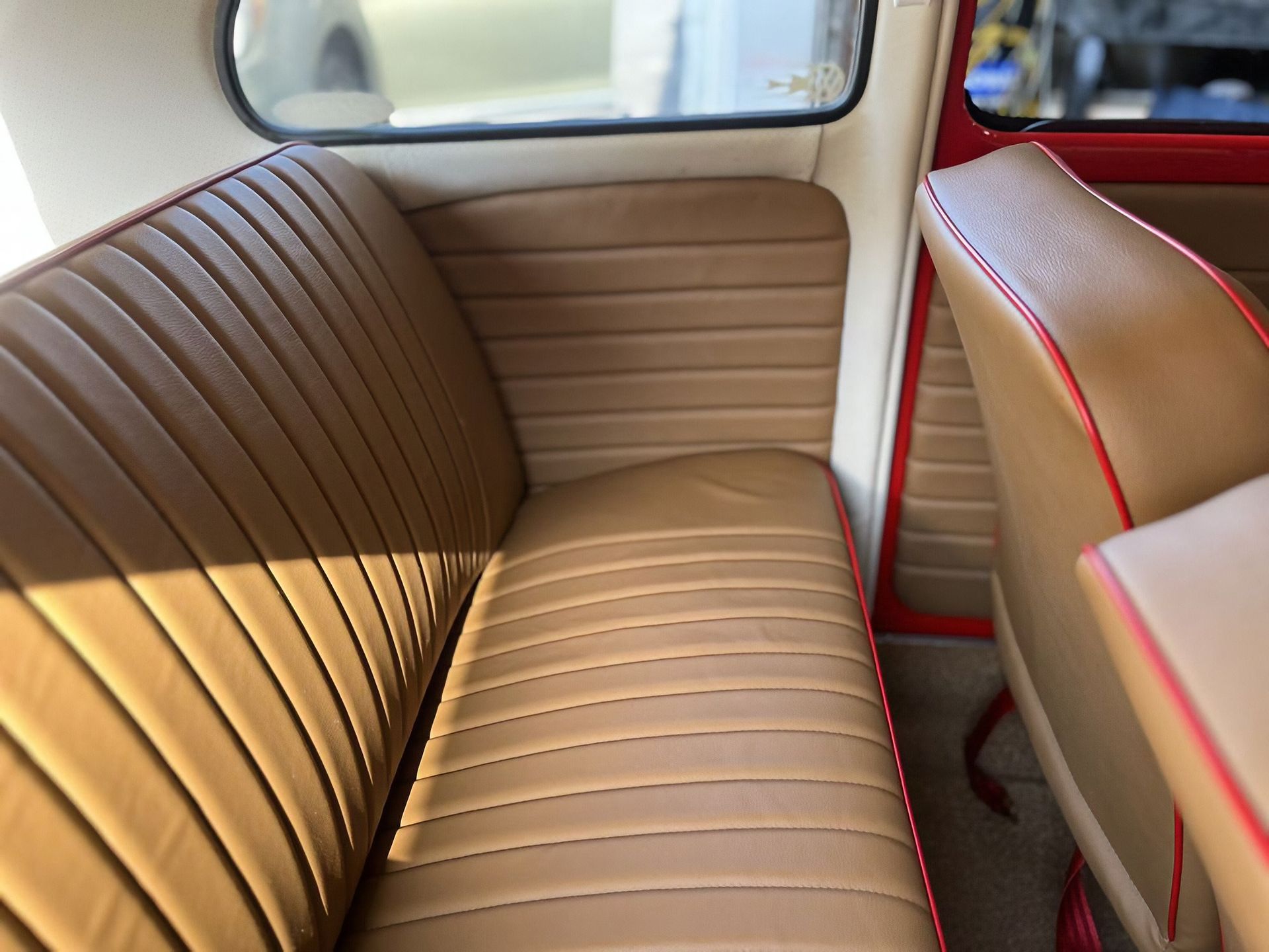 Tan vinyl car back seat with tan panels and red trim, lit by sunlight through the window.