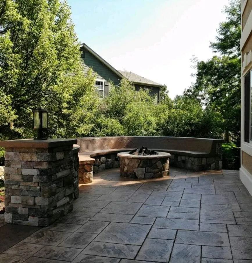 Stone patio with curved bench, fire pit, and trees beside a house