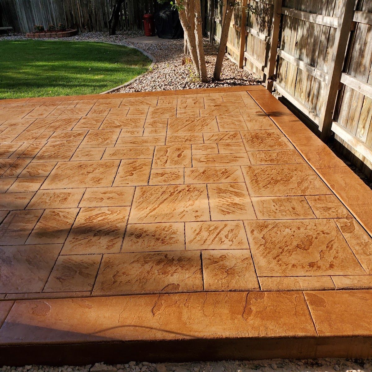Stamped concrete patio with a brown stone pattern, in a backyard.