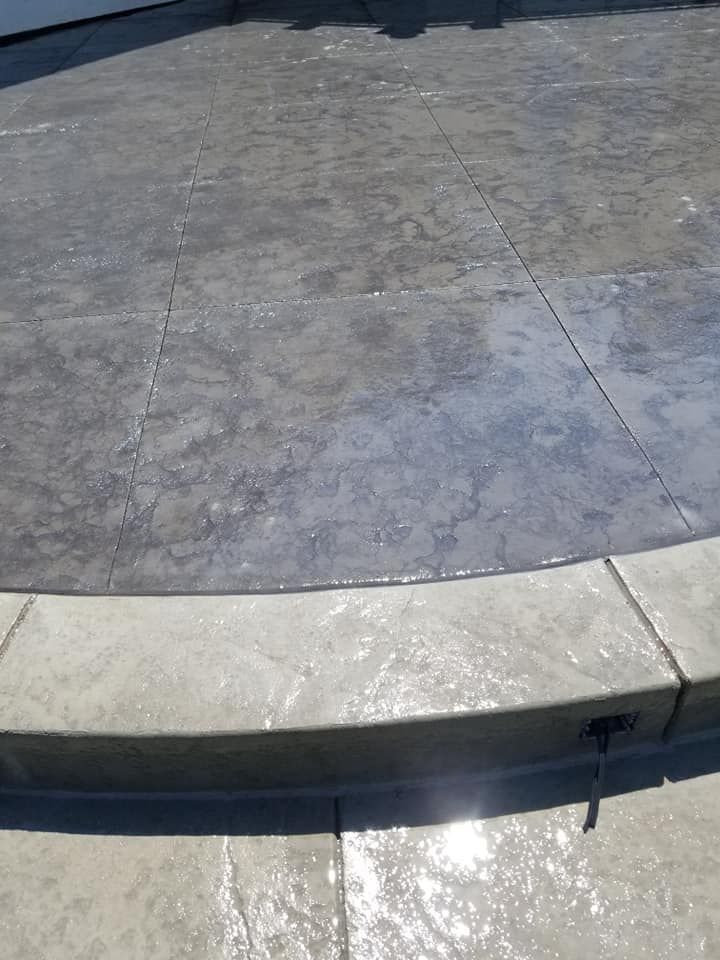 Gray concrete patio with rounded edge and step. Sunlight reflects off the wet surface.