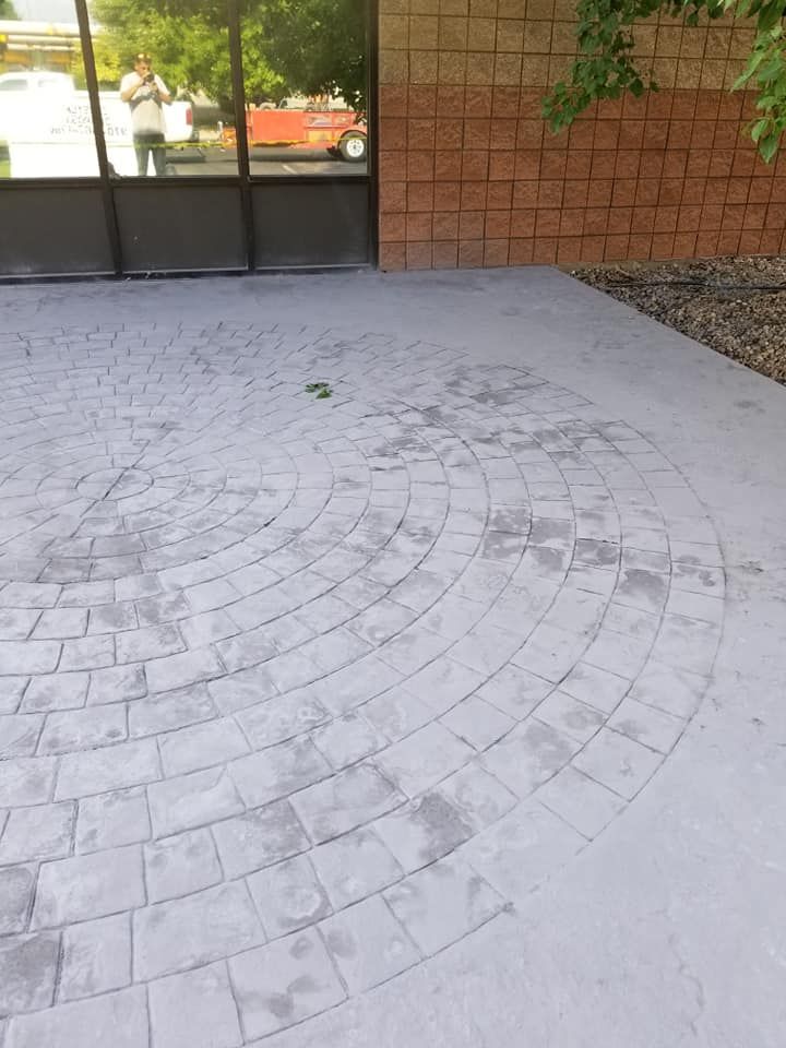 Circular brick pattern on a gray concrete patio in front of a building with a brick accent wall.