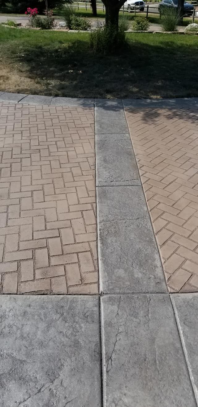 Sidewalk with brick pattern and grey border, next to grass and a tree.