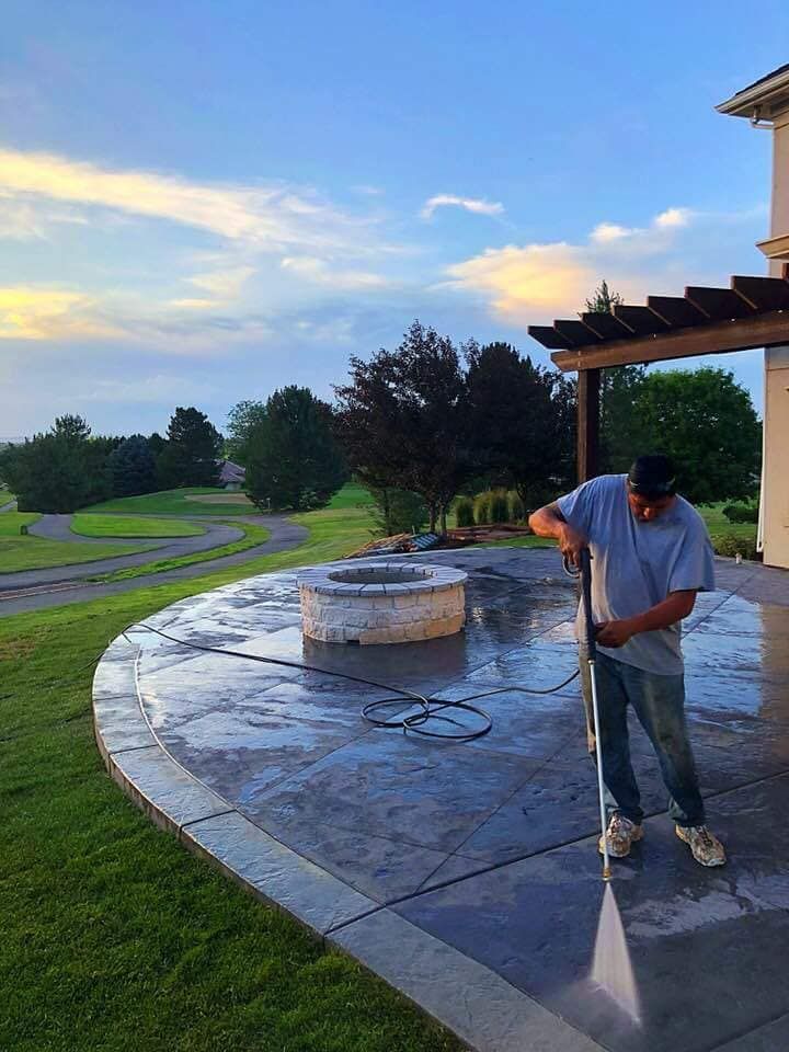 Man power washing a stone patio with fire pit and golf course view at sunset.
