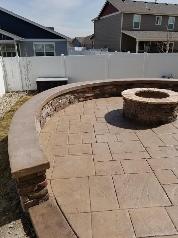 Curved patio with stone fire pit, stone and concrete walls, and stamped concrete flooring in backyard.