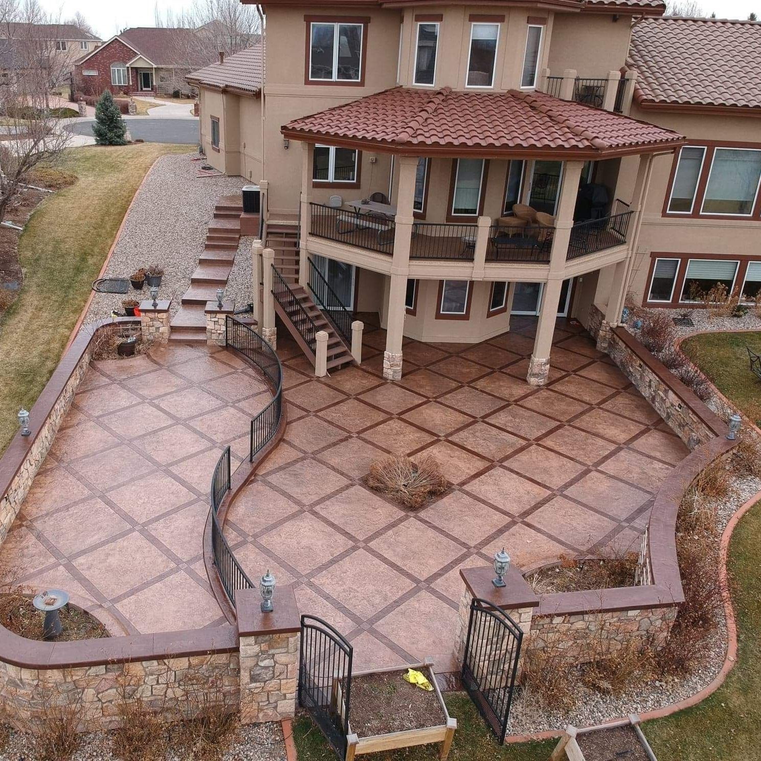 Backyard patio with stamped concrete, low walls, and a multi-story house.