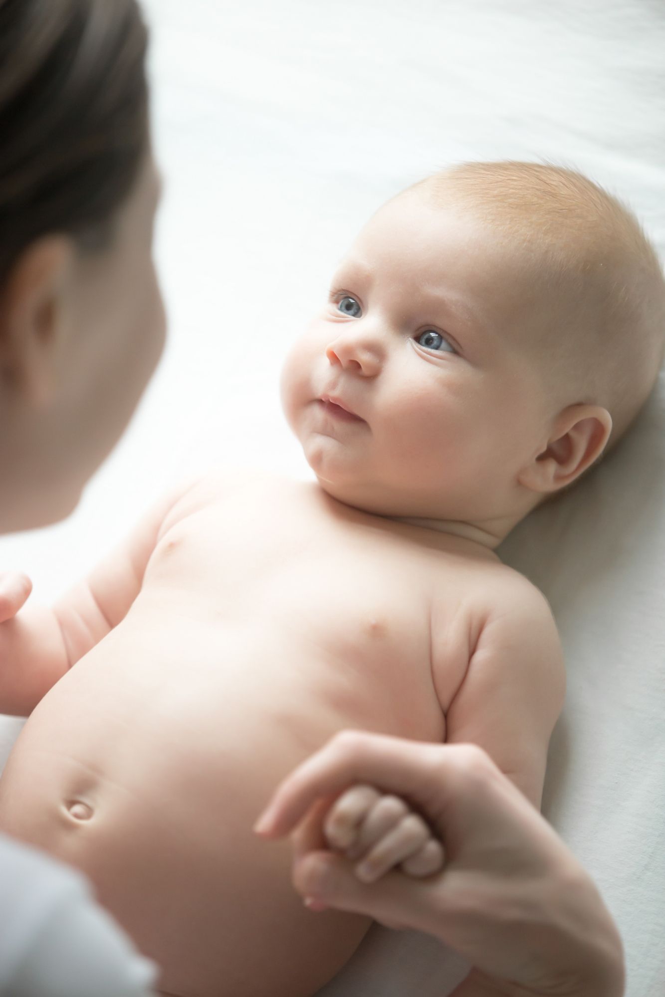 Bébé regardant une personne, tenant une main, allongé sur une surface blanche.