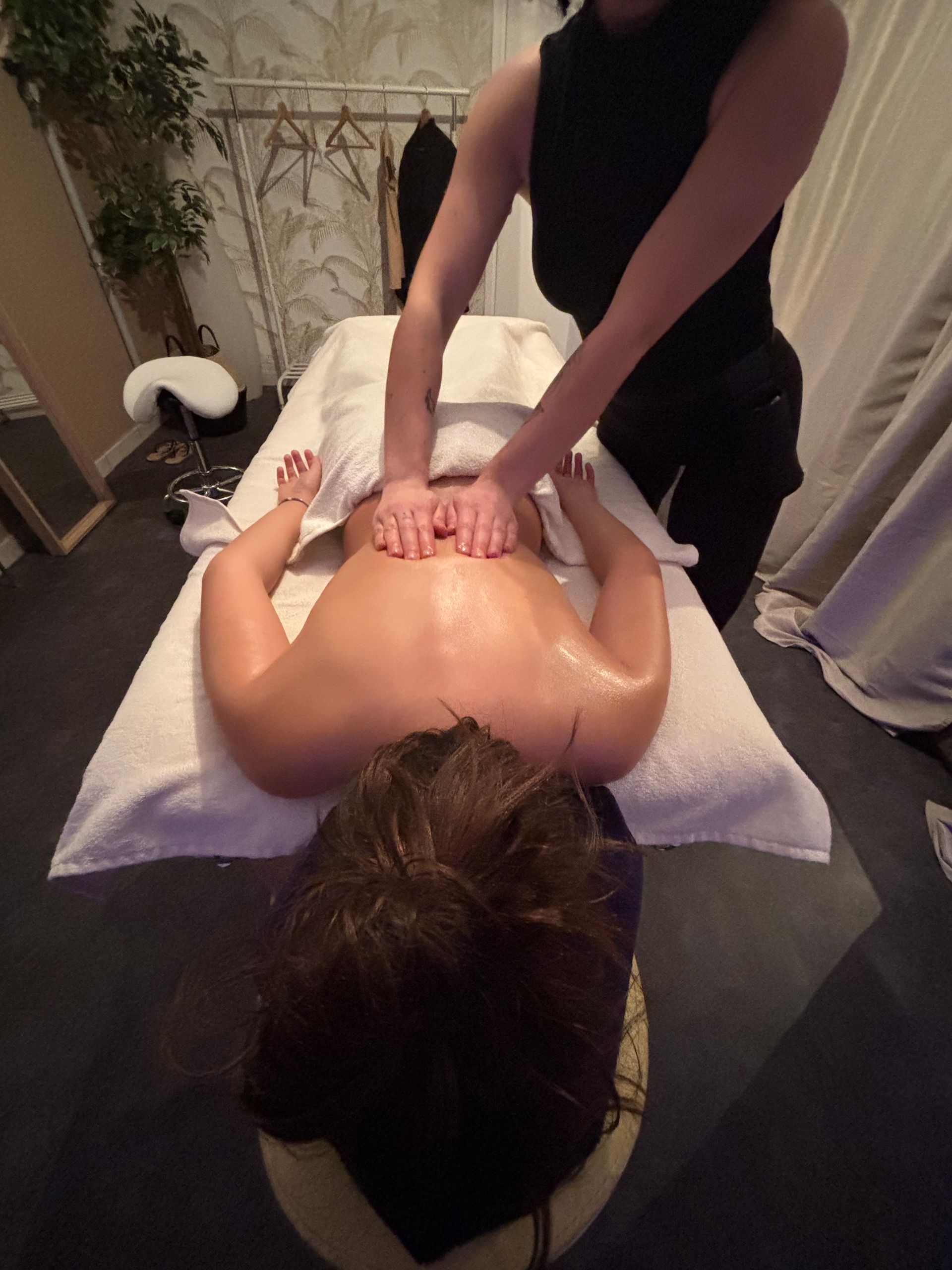 Une femme reçoit un massage du dos, allongée sur le ventre sur une table de massage. Les mains du thérapeute sont posées sur son dos.