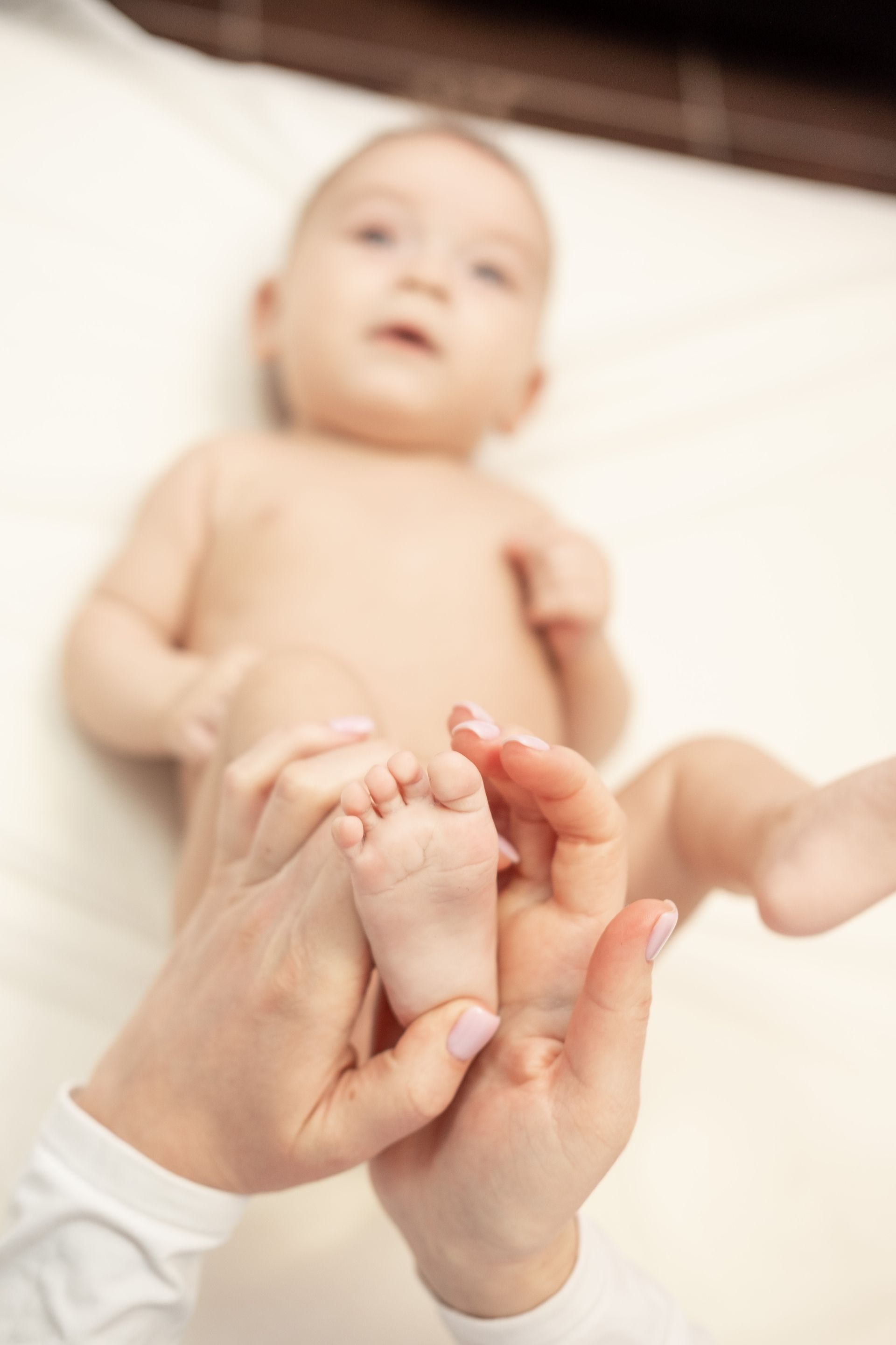 Des mains massent doucement le pied d'un bébé sur une surface blanche ; le bébé regarde vers le haut.