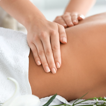 Des mains massent le dos d'une personne, dans un cadre de spa, avec une serviette blanche et des fleurs.