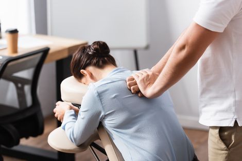 Une personne reçoit un massage des épaules assise dans un fauteuil de massage, dans un bureau.