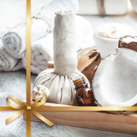 Un décor de spa avec serviettes, noix de coco, flacon d'huile et compresse aux herbes, le tout enveloppé d'un ruban doré.