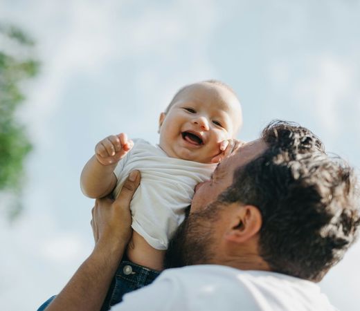 A man is holding a baby in his arms and kissing it on the cheek.