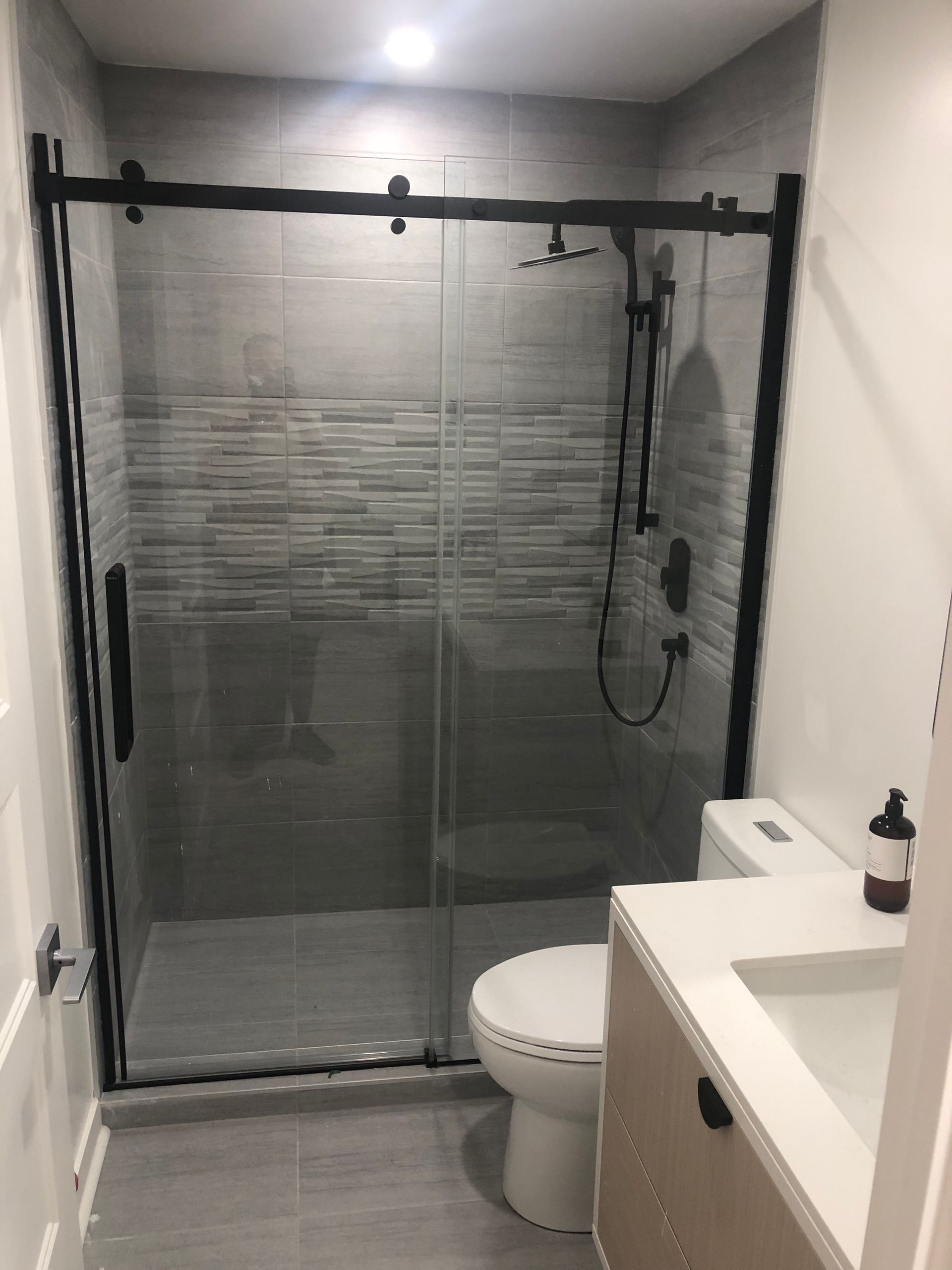 Une salle de bain avec WC , lavabo et douche avec porte coulissante vitrée.