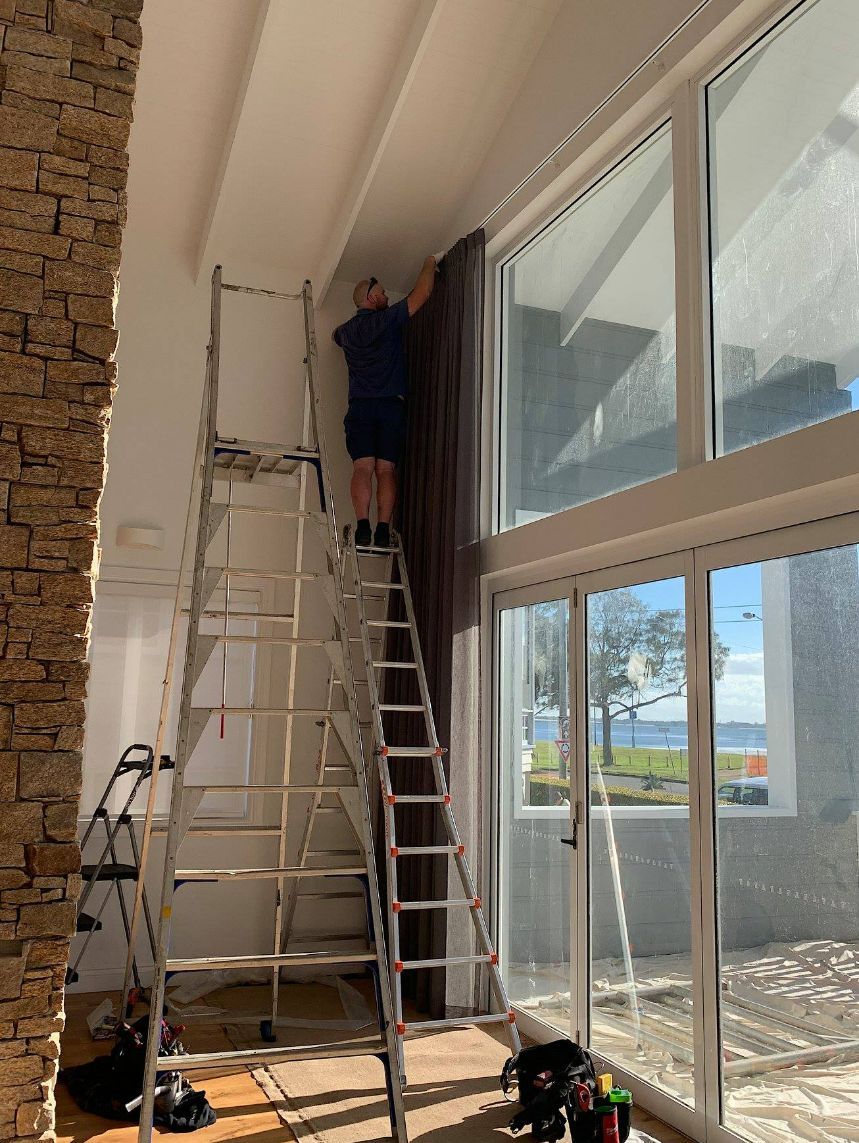 Man On A Ladder Installing Motorised Curtains — Studio Curtains & Blinds in Mount Gravatt, QLD