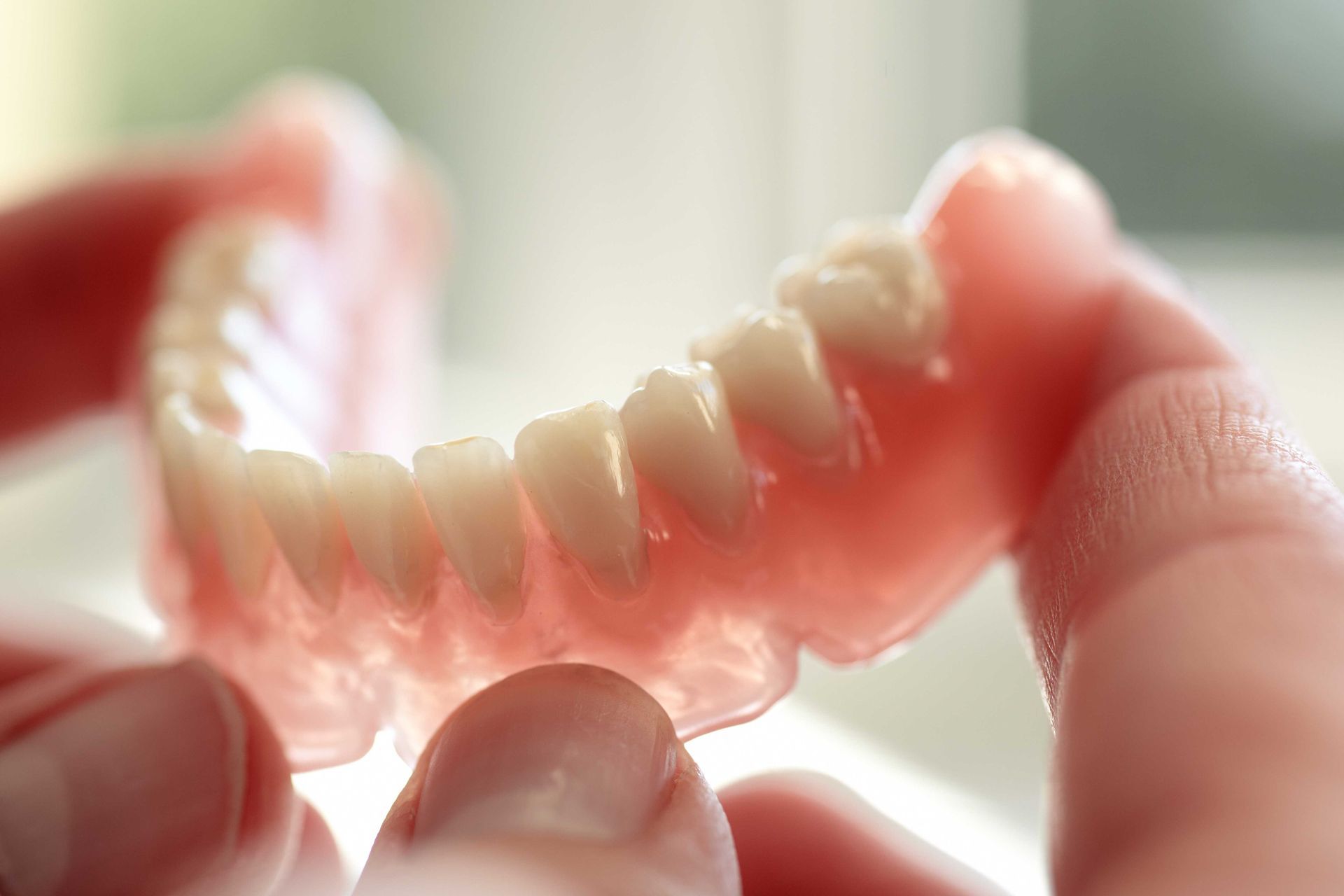 A set of dentures held by two hands, showing a row of upper teeth.