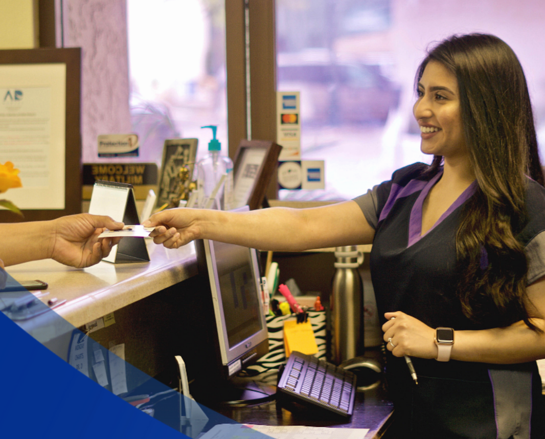 Woman at dental office counter taking a card, smiling. 