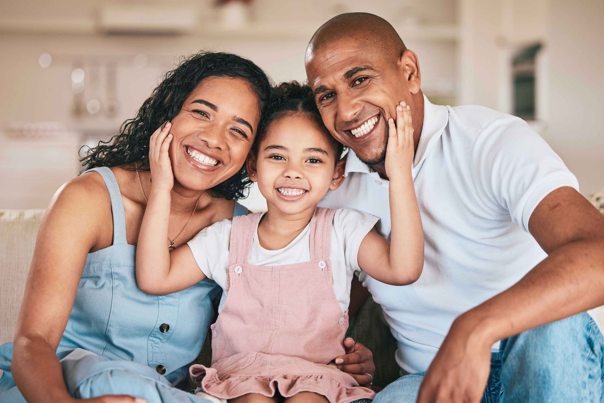 Family of three smiles for the camera, touching their faces. 