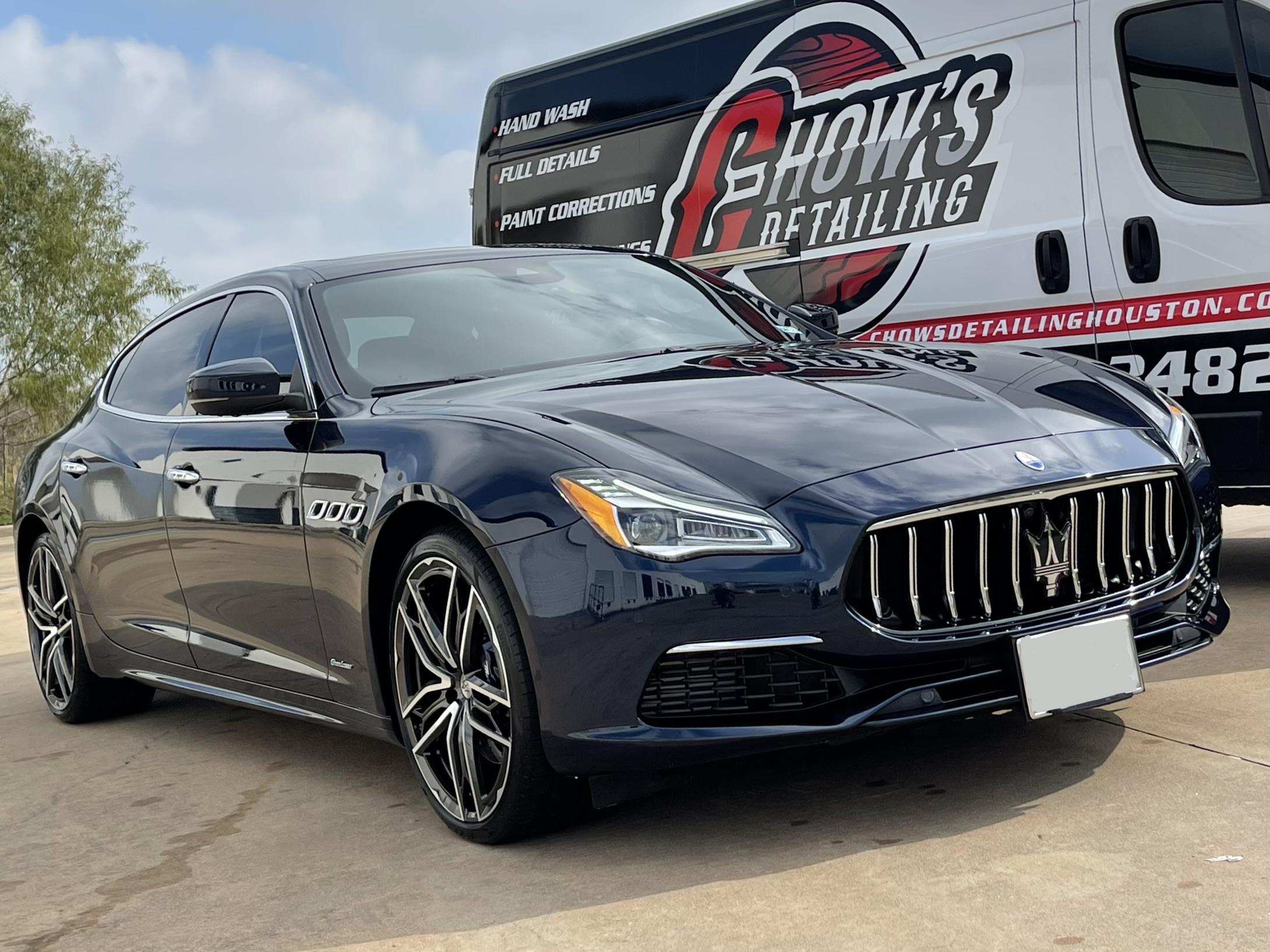 a black maserati is parked in front of a white van .